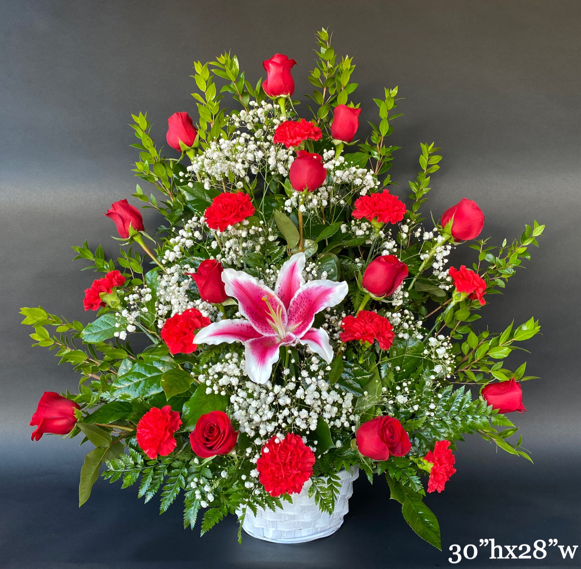 Red roses and carnations with a pink lily in a white basket