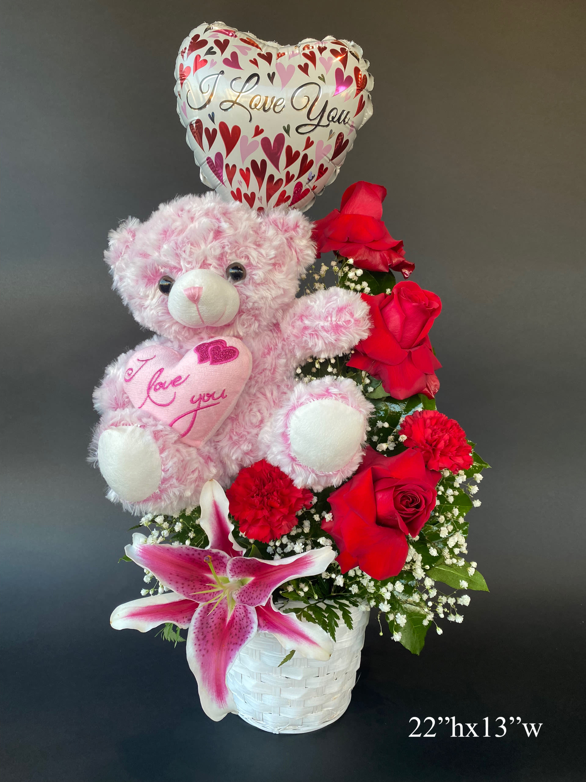 Pink teddy bear with heart balloon and red roses in a white basket