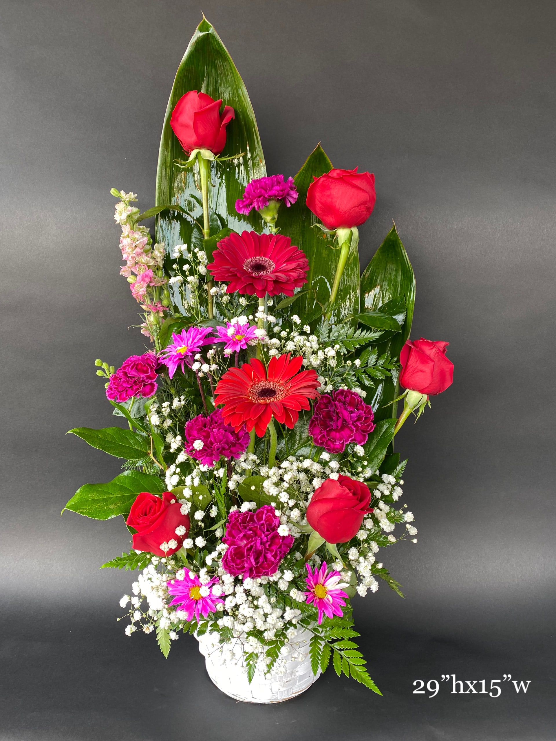 Tall mixed bouquet with red roses and pink gerbera daisies in a white basket