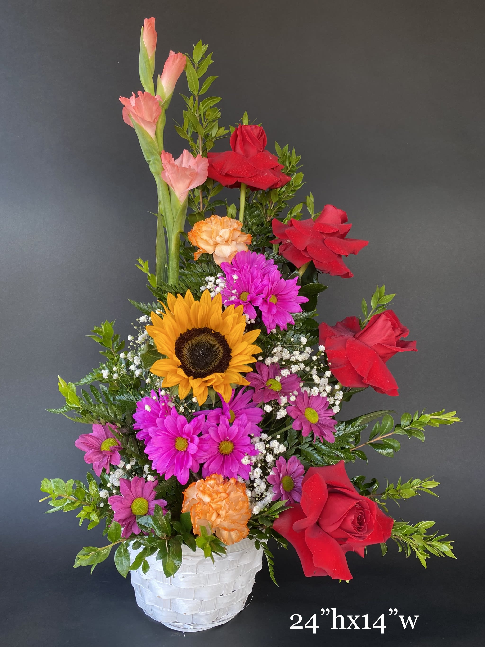 Mixed flower arrangement in a white basket with red roses and sunflowers