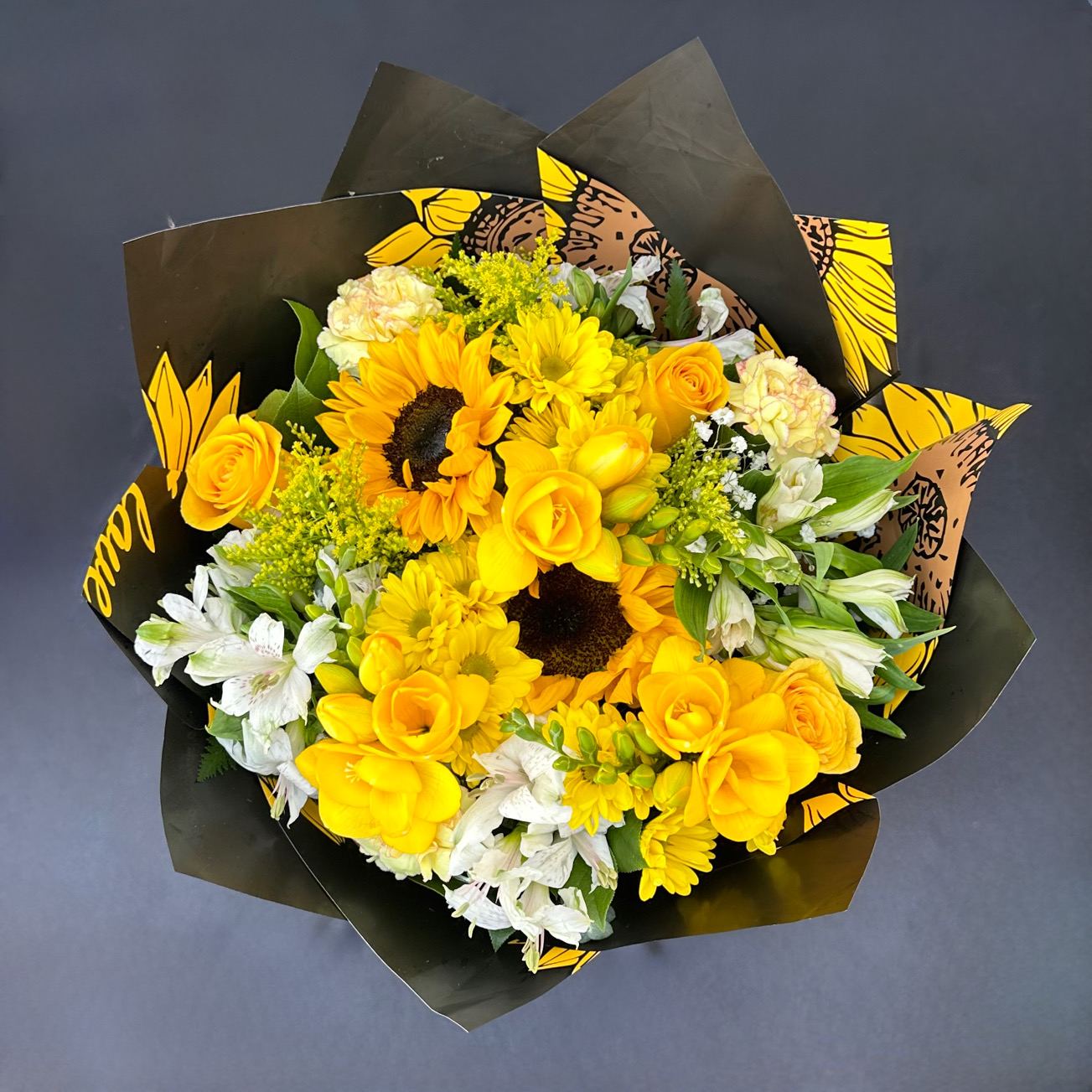 Bouquet of yellow roses, sunflowers, and white alstroemeria in black wrap