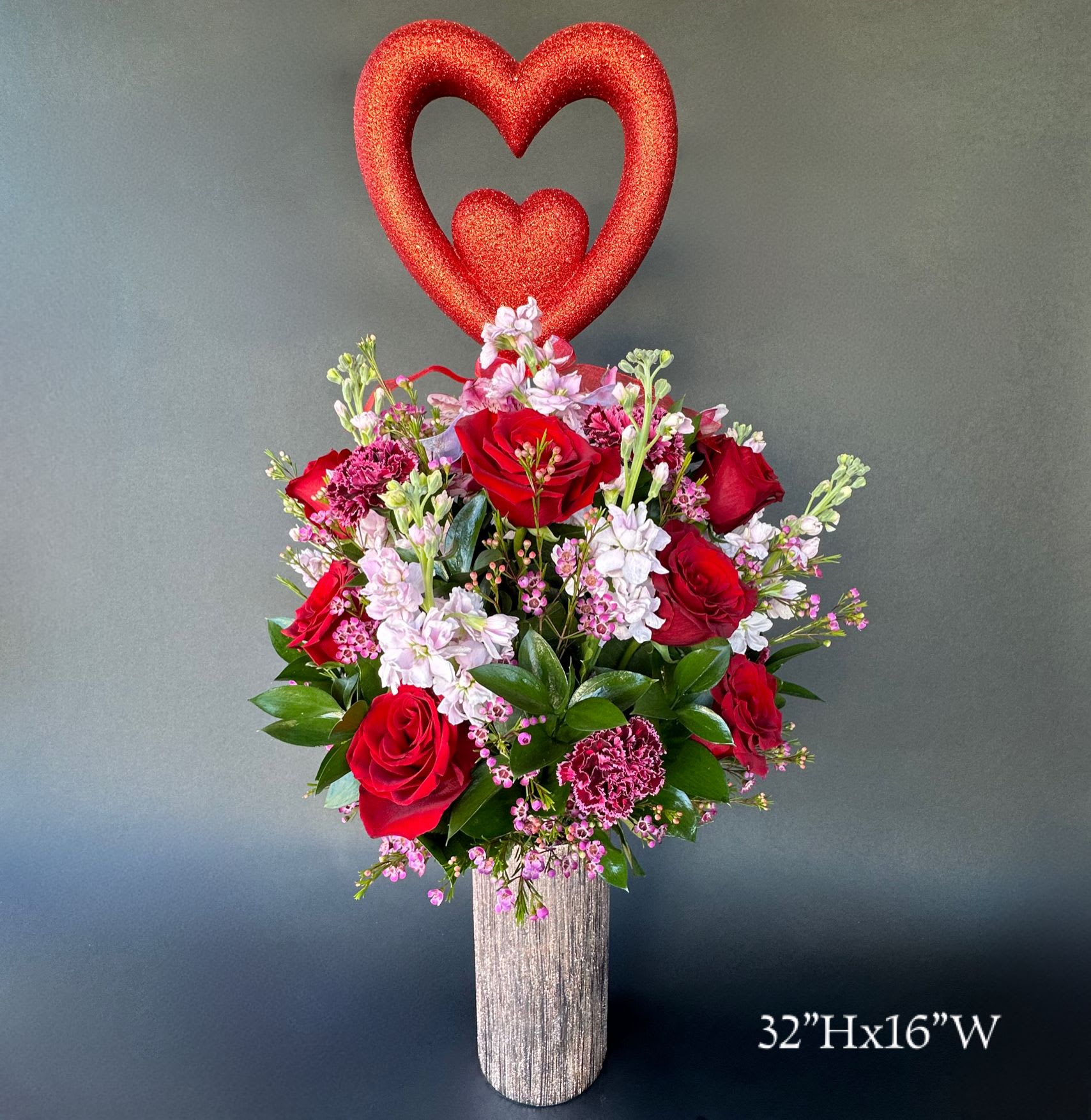 Red rose arrangement with a glittery heart topper in a tall vase