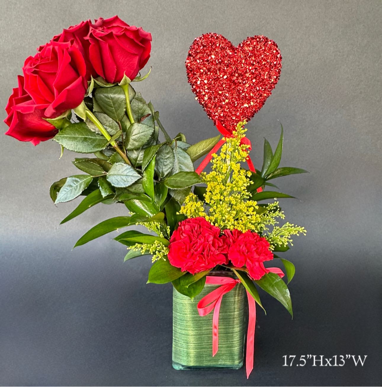 Red roses and carnations in a green vase with a glitter heart pick