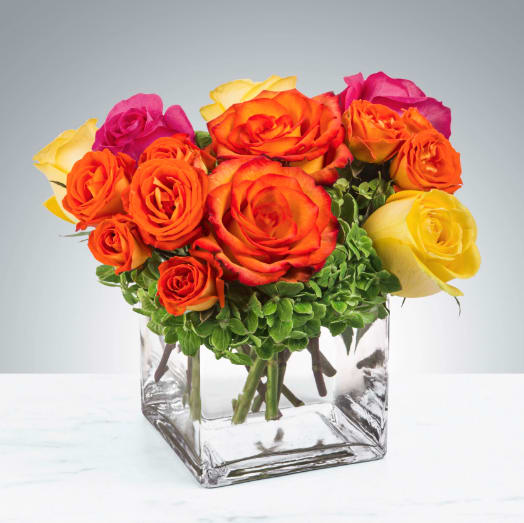 Bouquet of orange, yellow, and pink roses in a clear square vase