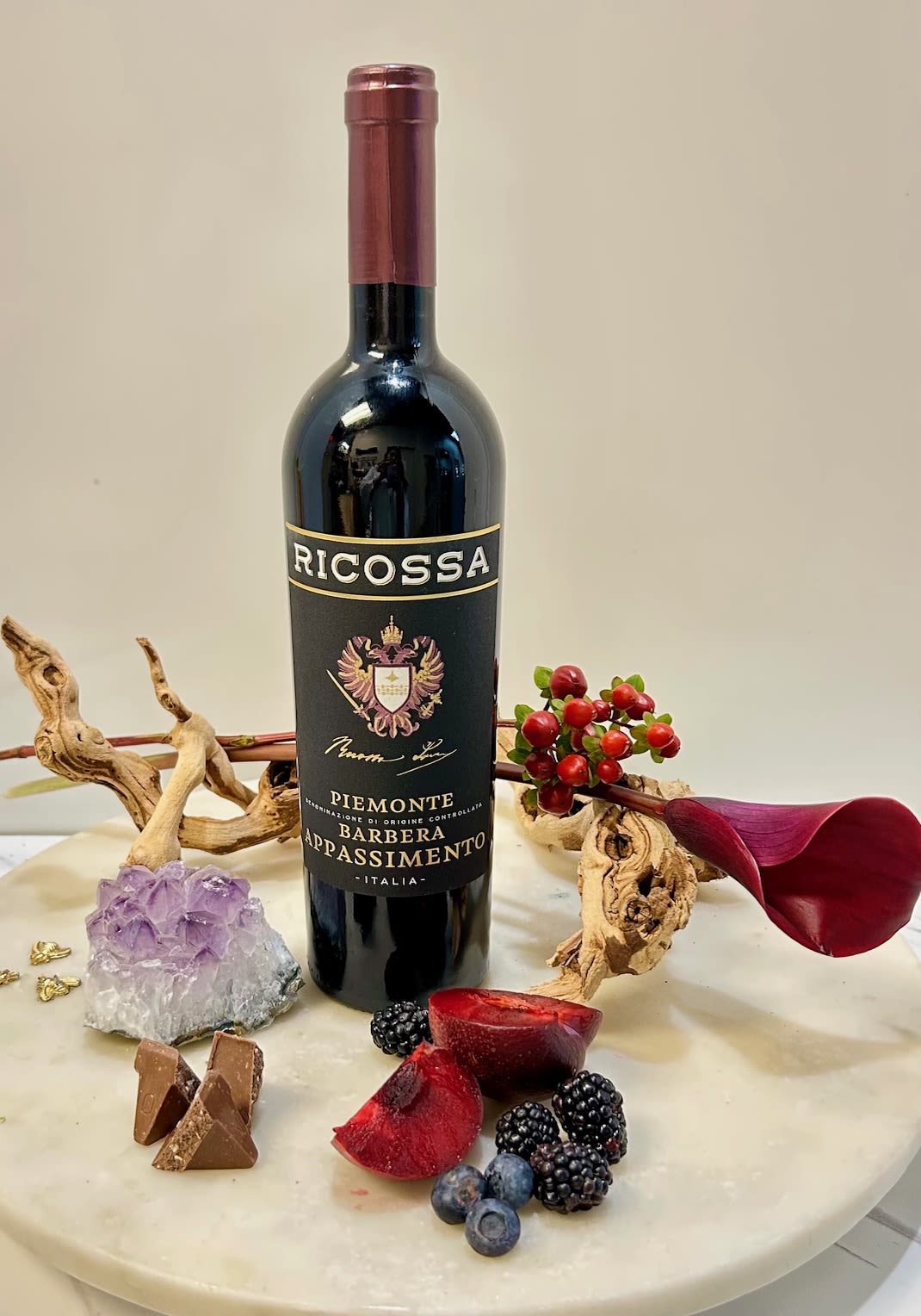 Wine bottle arranged with berries, chocolate, and a purple crystal on a round table