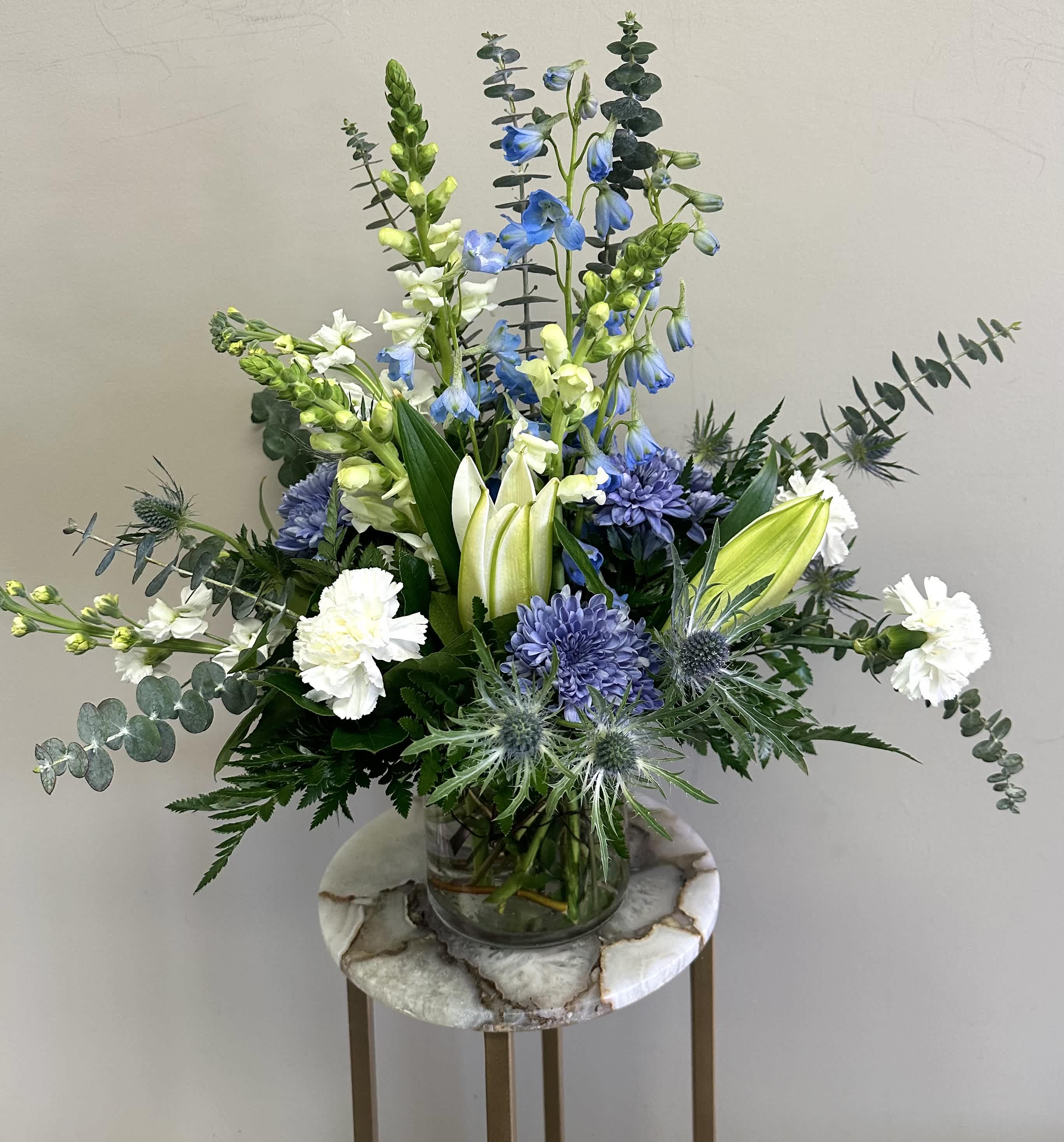 Arrangement of blue and white flowers with lilies and carnations in a clear glass vase