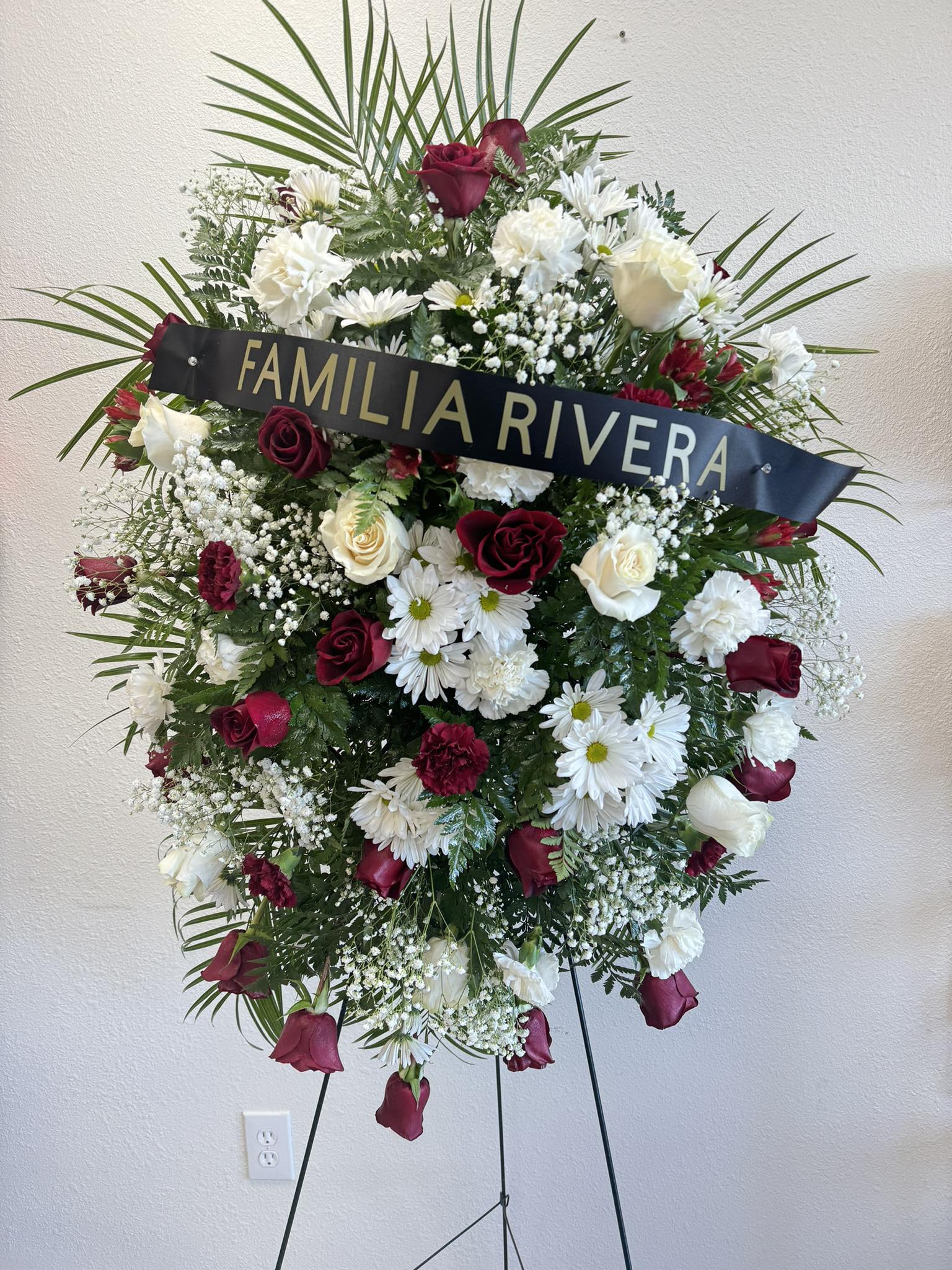 Standing funeral wreath of red and white flowers with a name ribbon