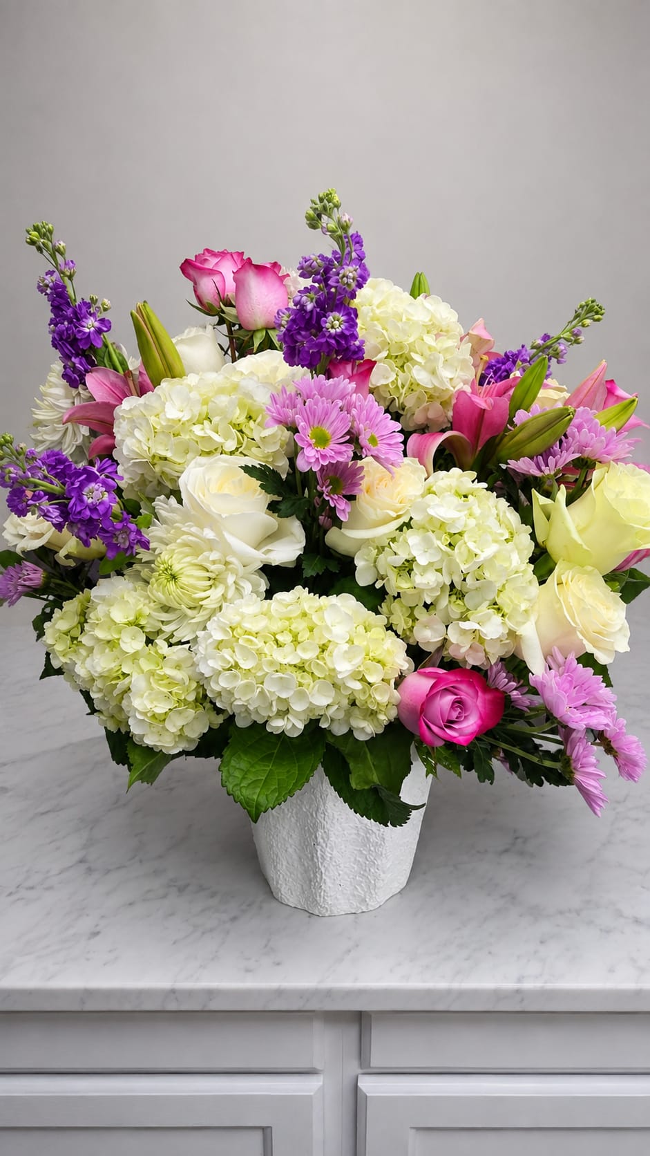 Mixed bouquet of pink, white, and purple flowers in a white vase