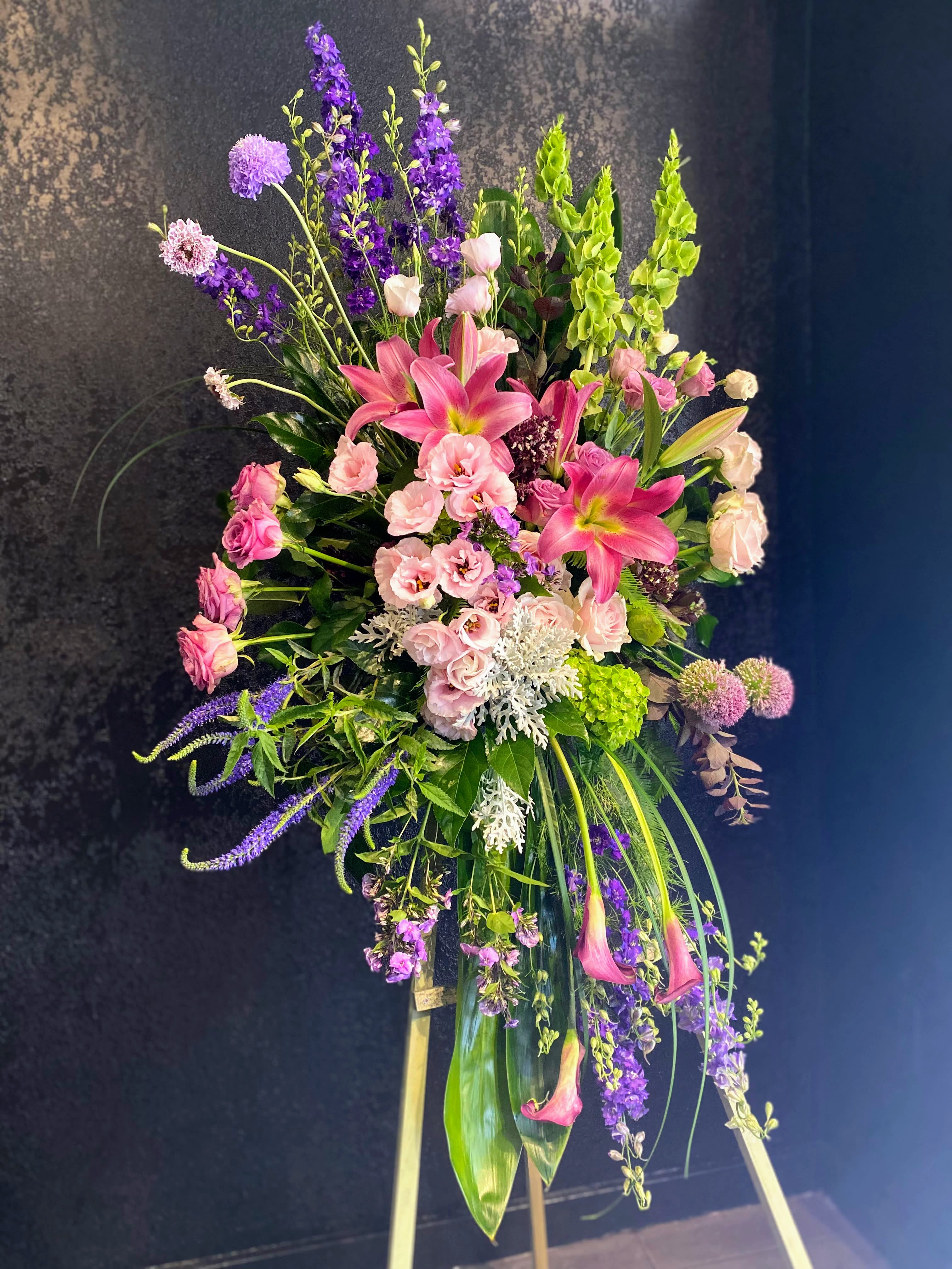 Tall standing spray of pink lilies and mixed purple flowers on a wooden easel.