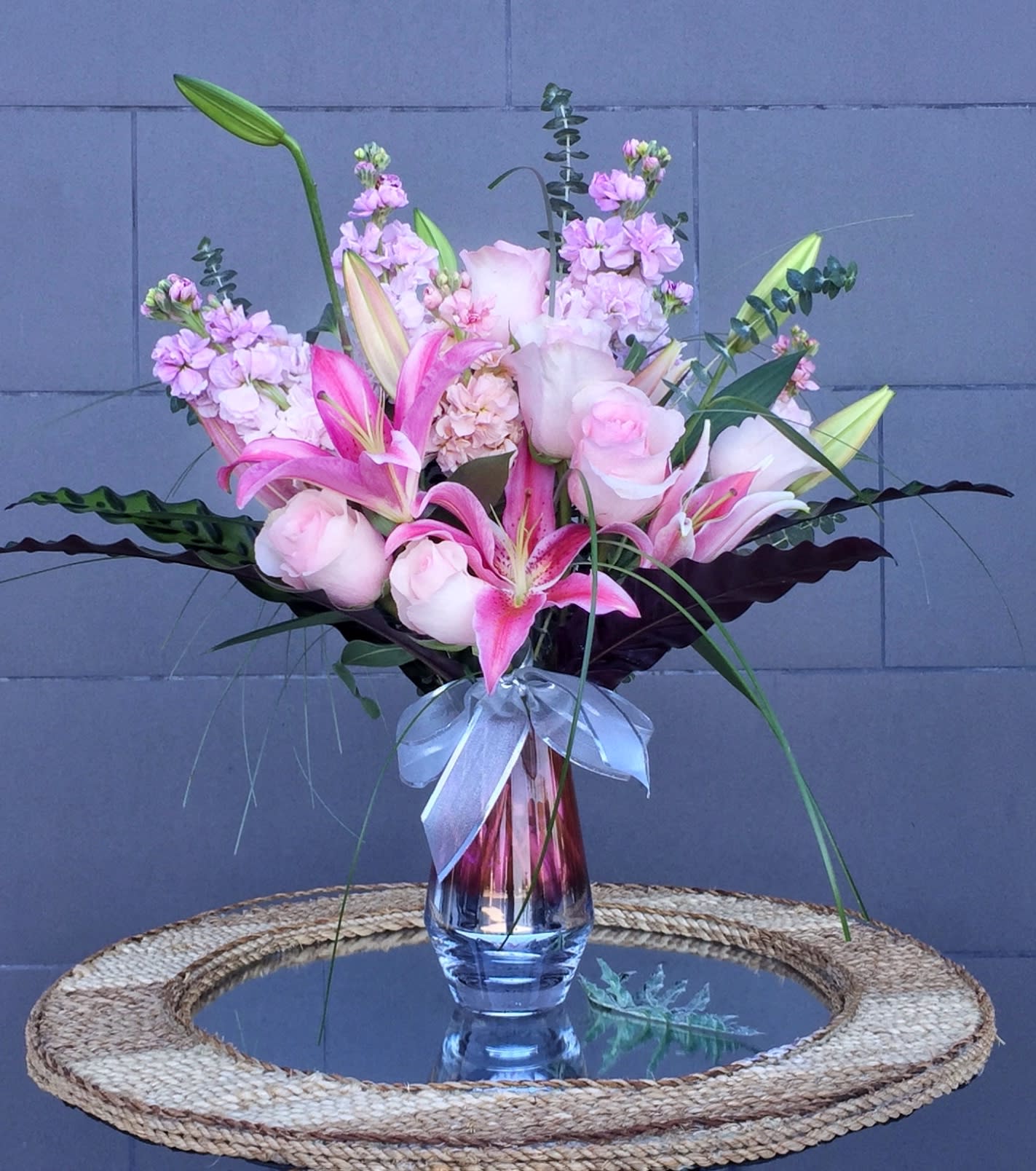 Pink lilies and roses arranged in a glass vase with a ribbon