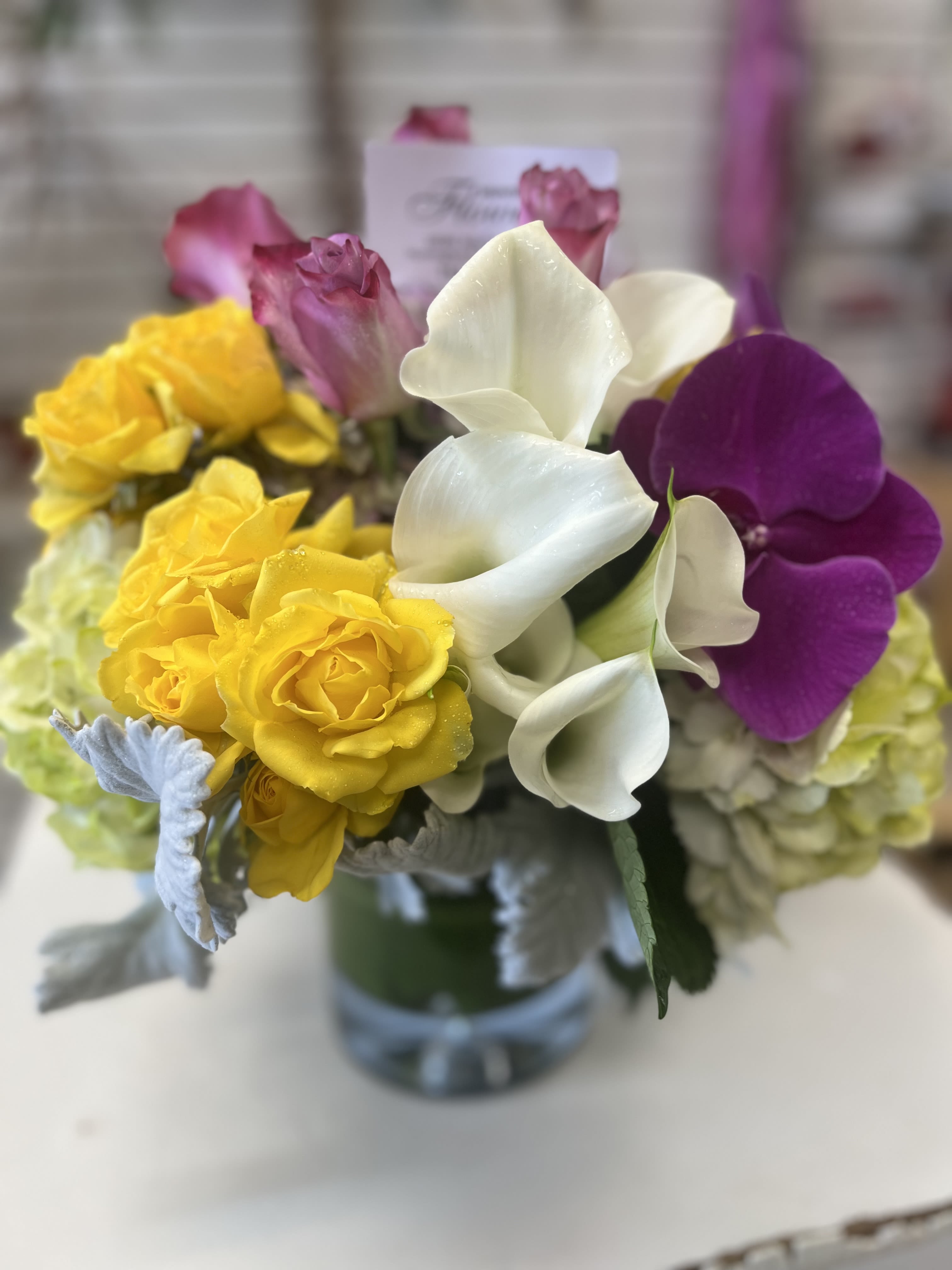 Bouquet of yellow roses, white calla lilies, and purple orchids in a glass vase