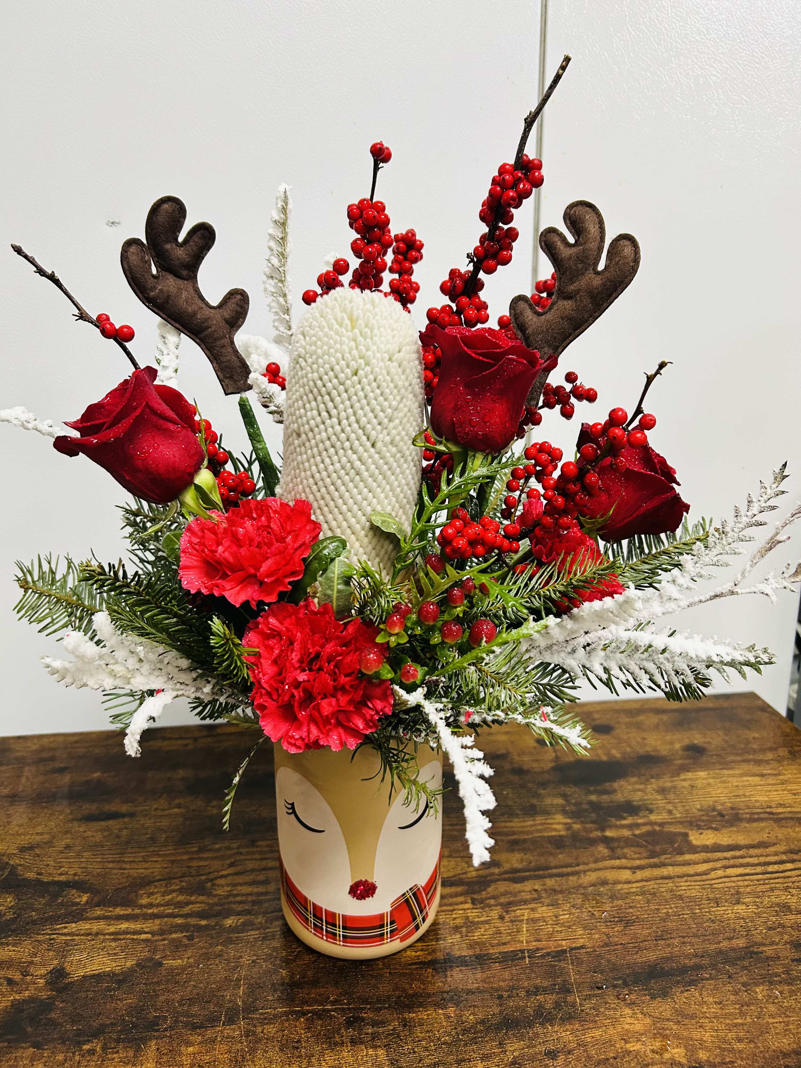 Holiday arrangement with red roses, carnations, and reindeer antlers in a decorative vase