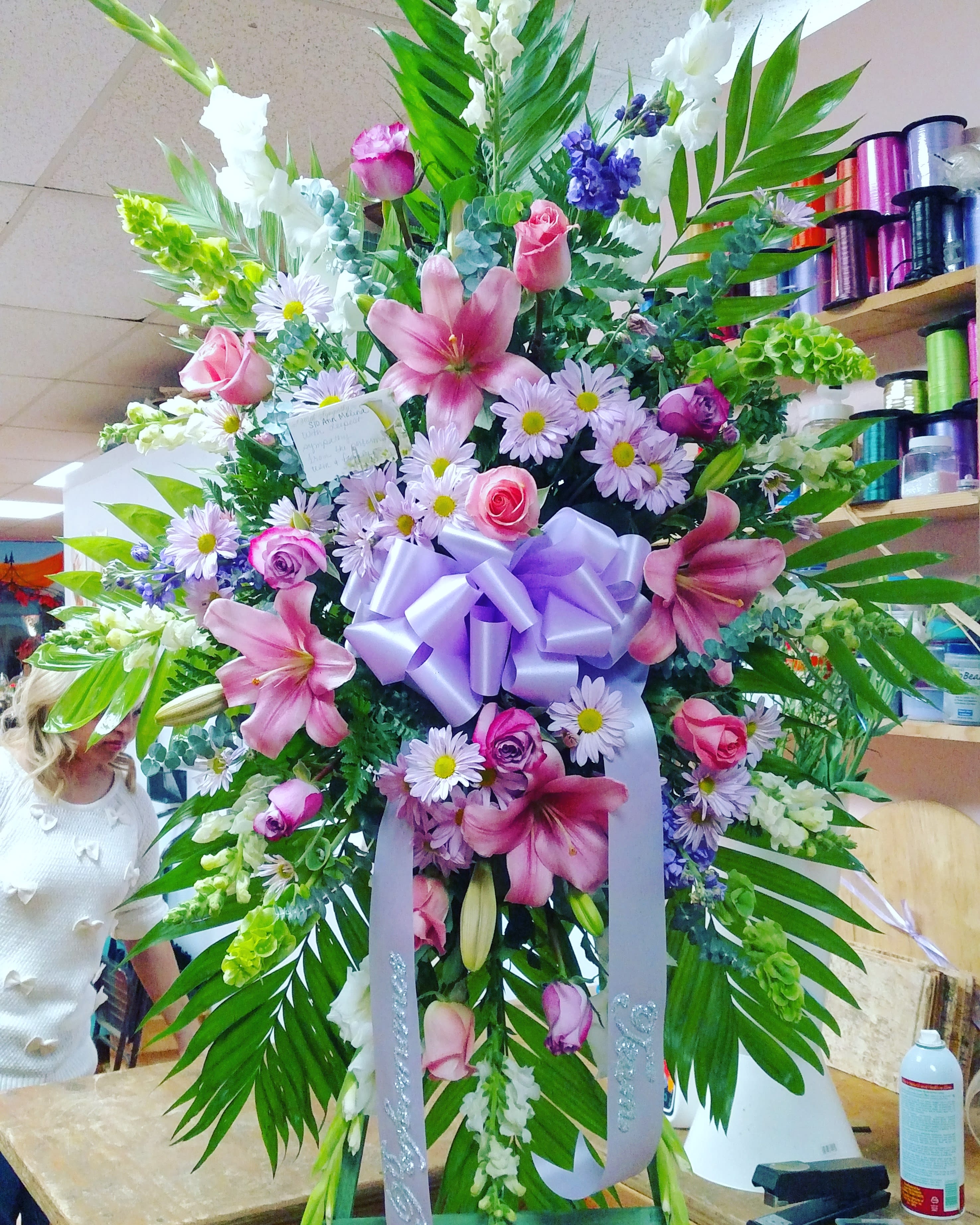 Large floral standing spray with pink lilies, roses, and daisies, tied with a lavender bow