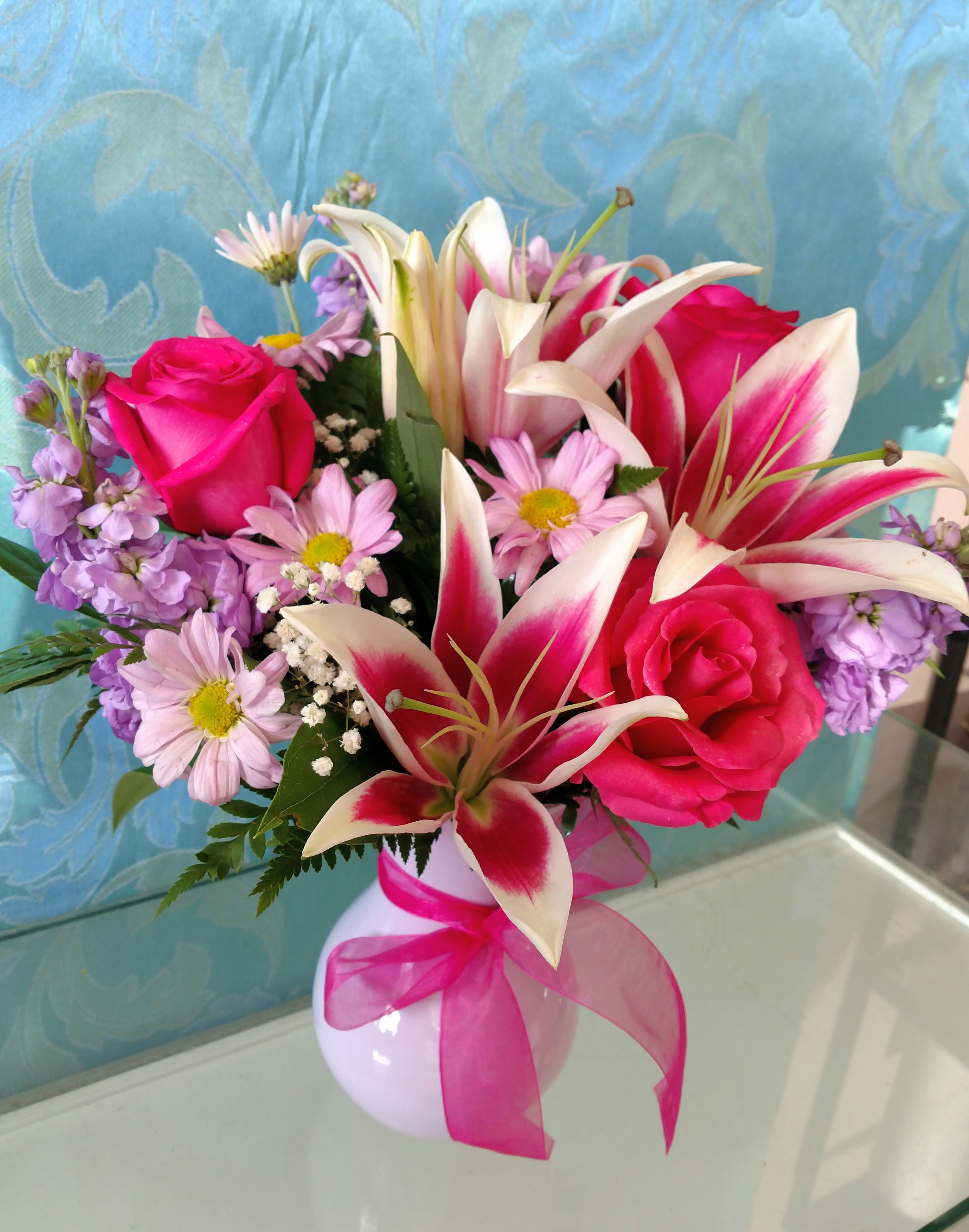 Pink roses and lilies in a white vase with a pink ribbon