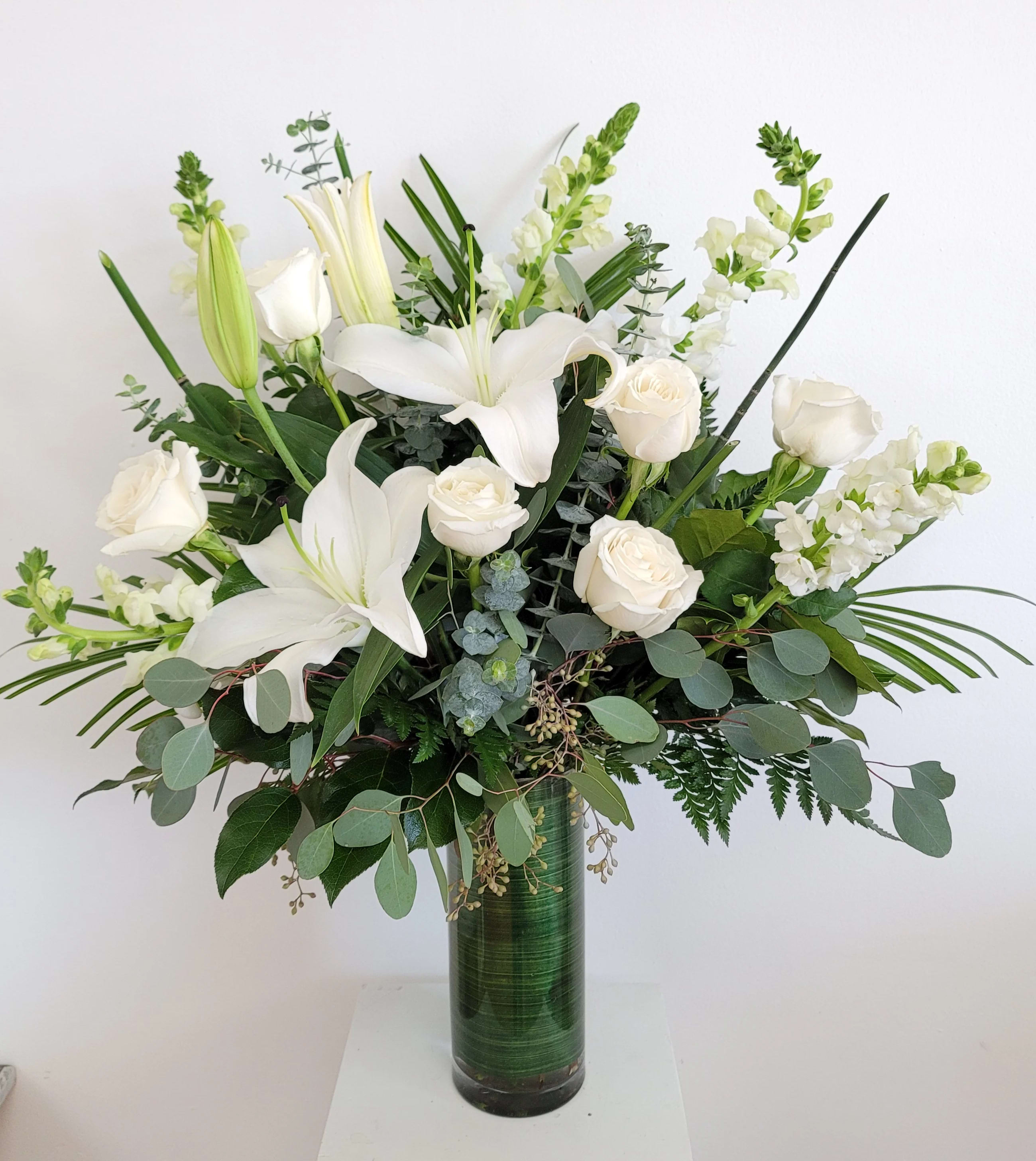White lilies and roses in a tall green glass vase
