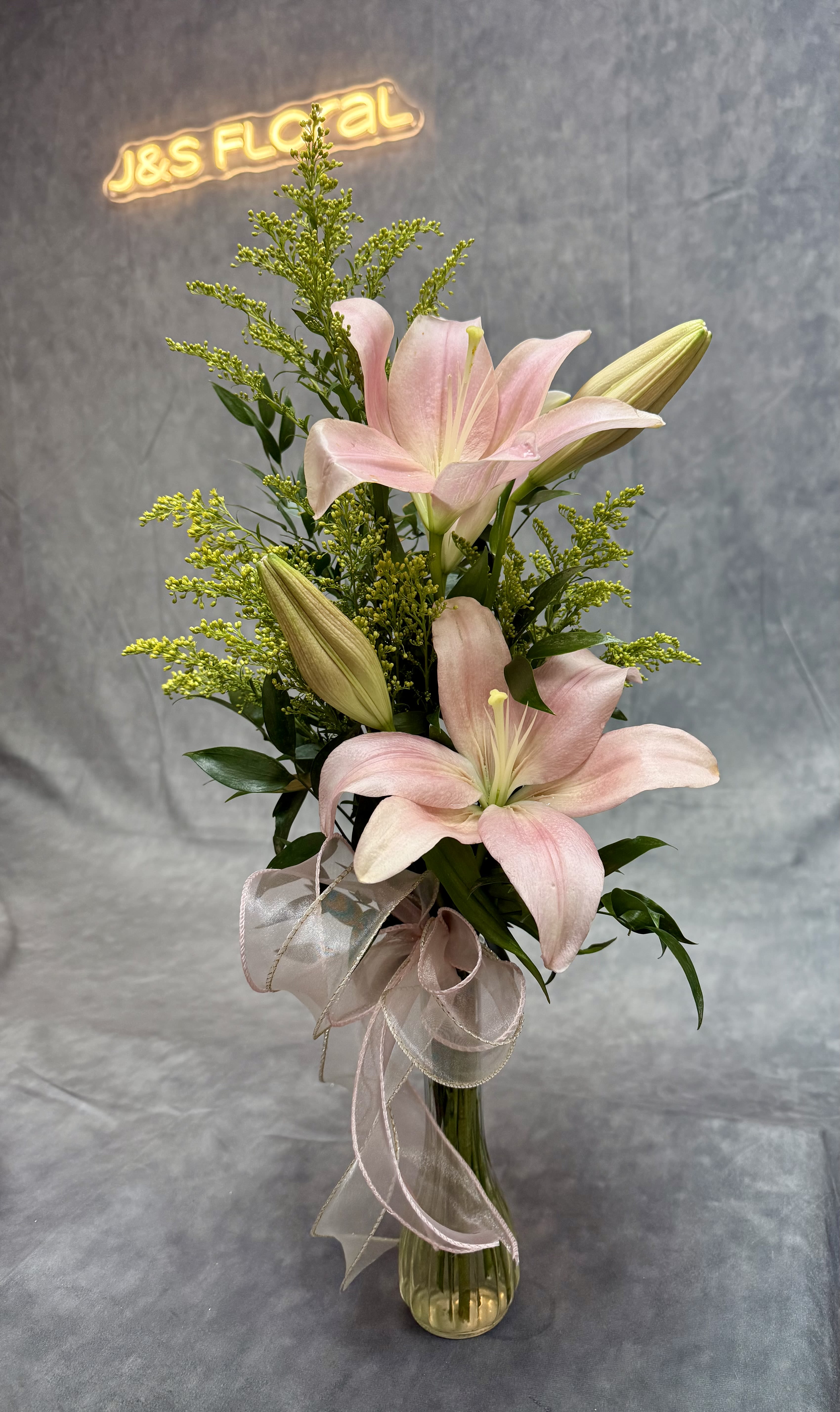 Pink lilies in a glass vase with a ribbon bow