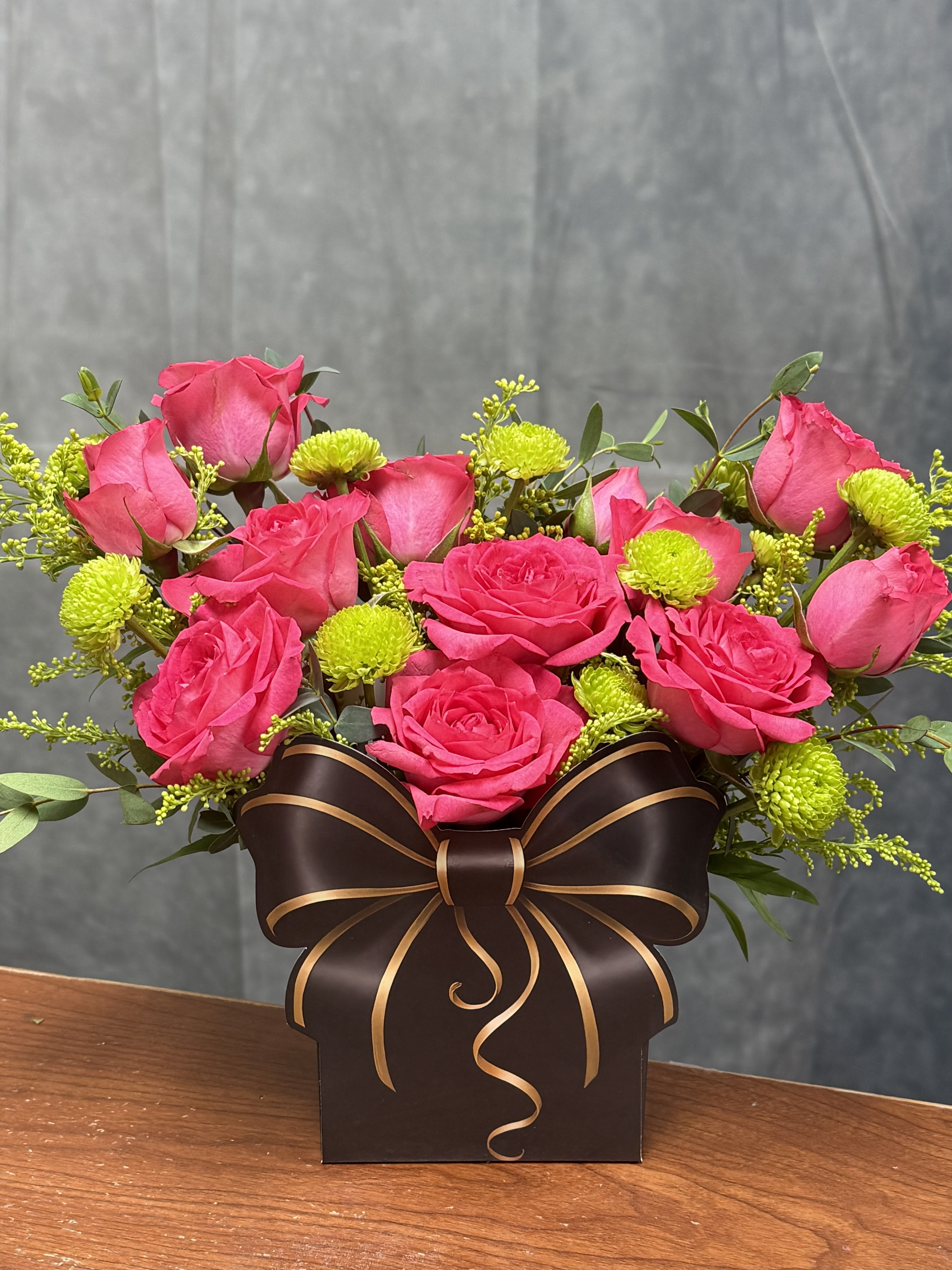 Pretty &amp; Bright Bow Bag - Bright, cheerful, and full of charm, our Pretty &amp; Bright Bow Bag features vibrant hot pink roses, playful green button mums, and fresh greenery beautifully arranged in a unique bow-shaped gift bag container. Designed to look like a beautifully wrapped present, this eye-catching arrangement is perfect for birthdays, celebrations, thank-you gifts, or simply making someone’s day a little brighter.  Flowers and greenery may vary based on seasonal availability and freshness while maintaining the same overall color palette, style, and value. 