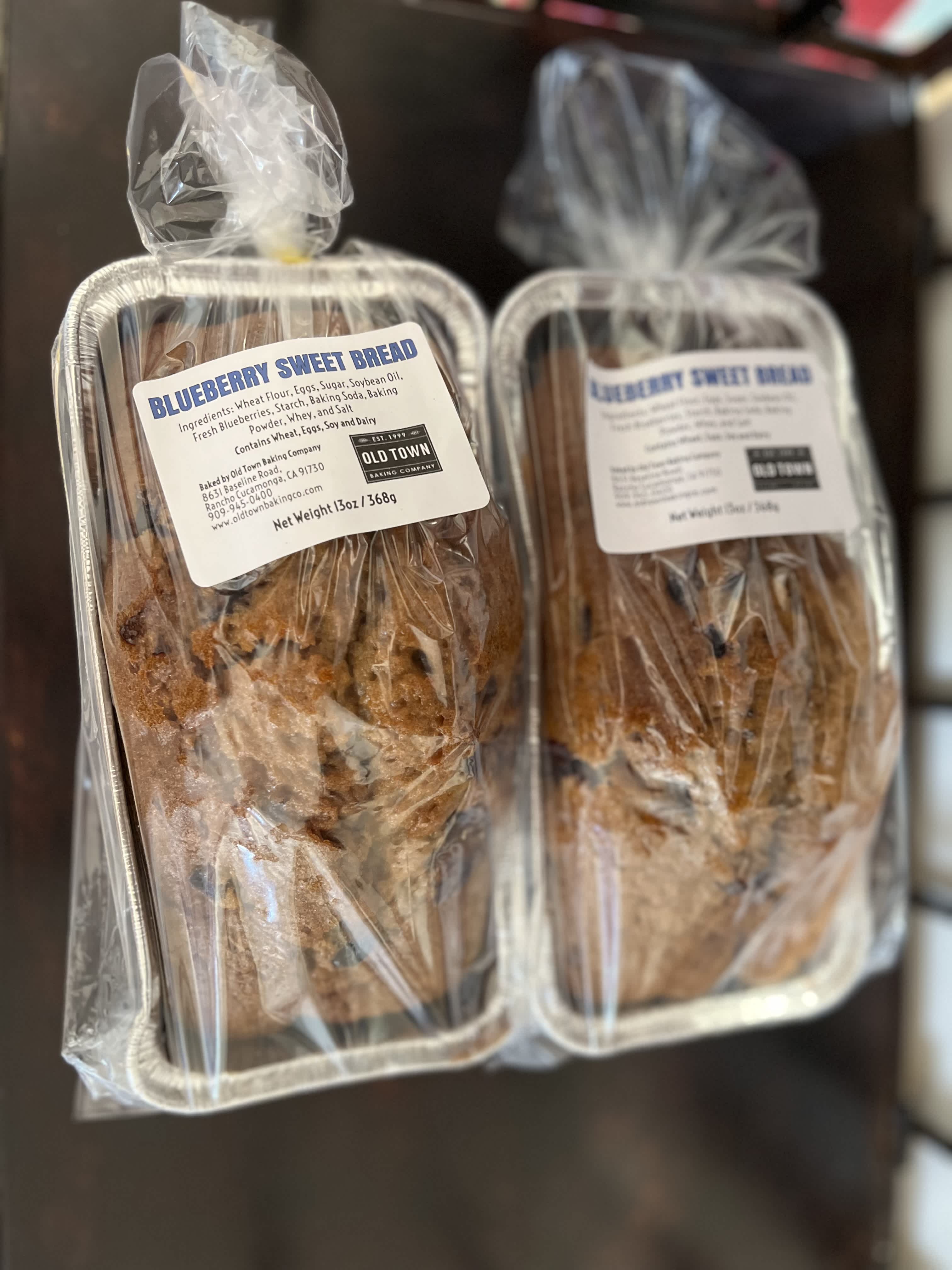 Two wrapped blueberry sweet bread loaves in foil pans