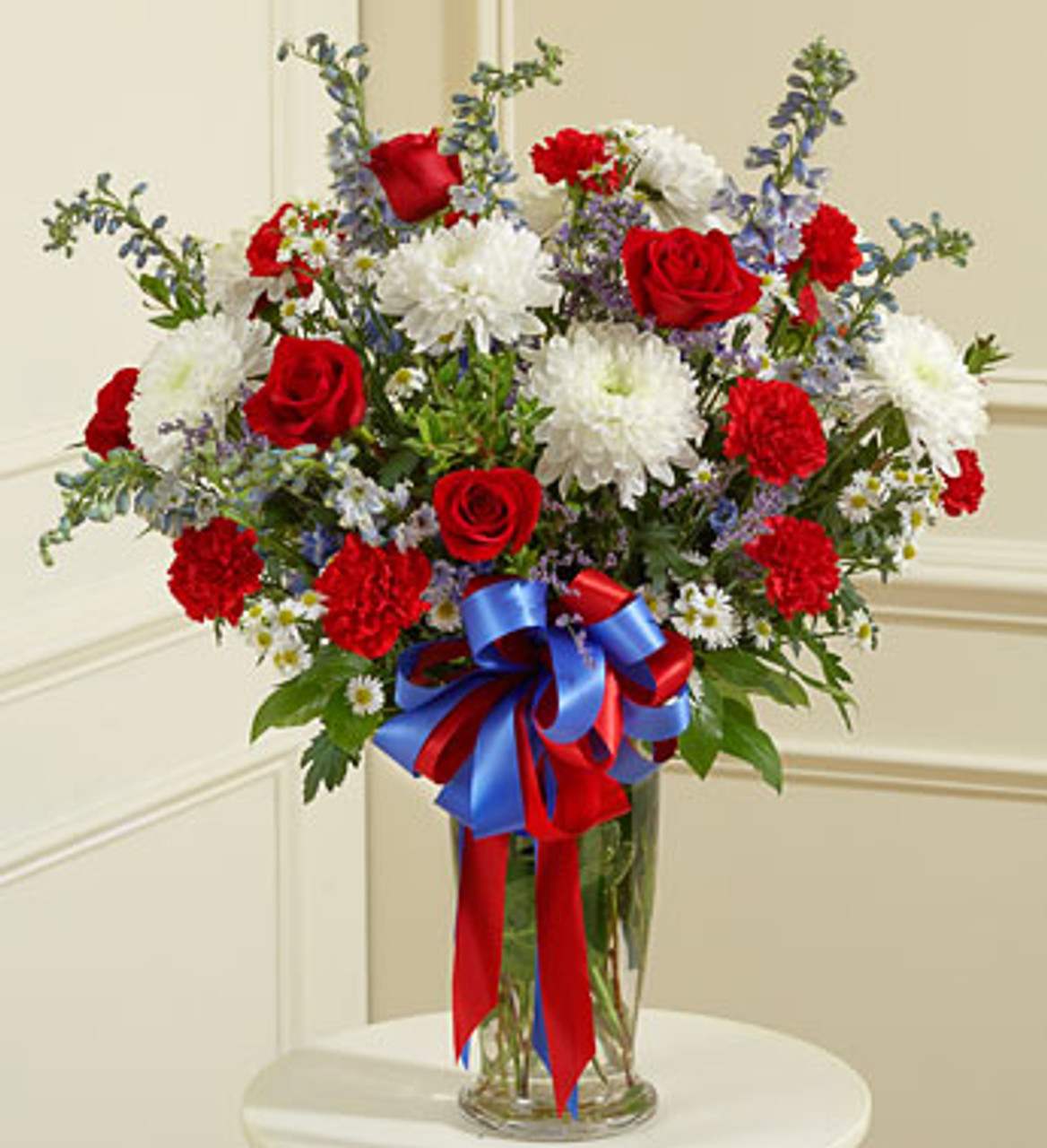Red roses and white chrysanthemums in a glass vase with a red and blue ribbon