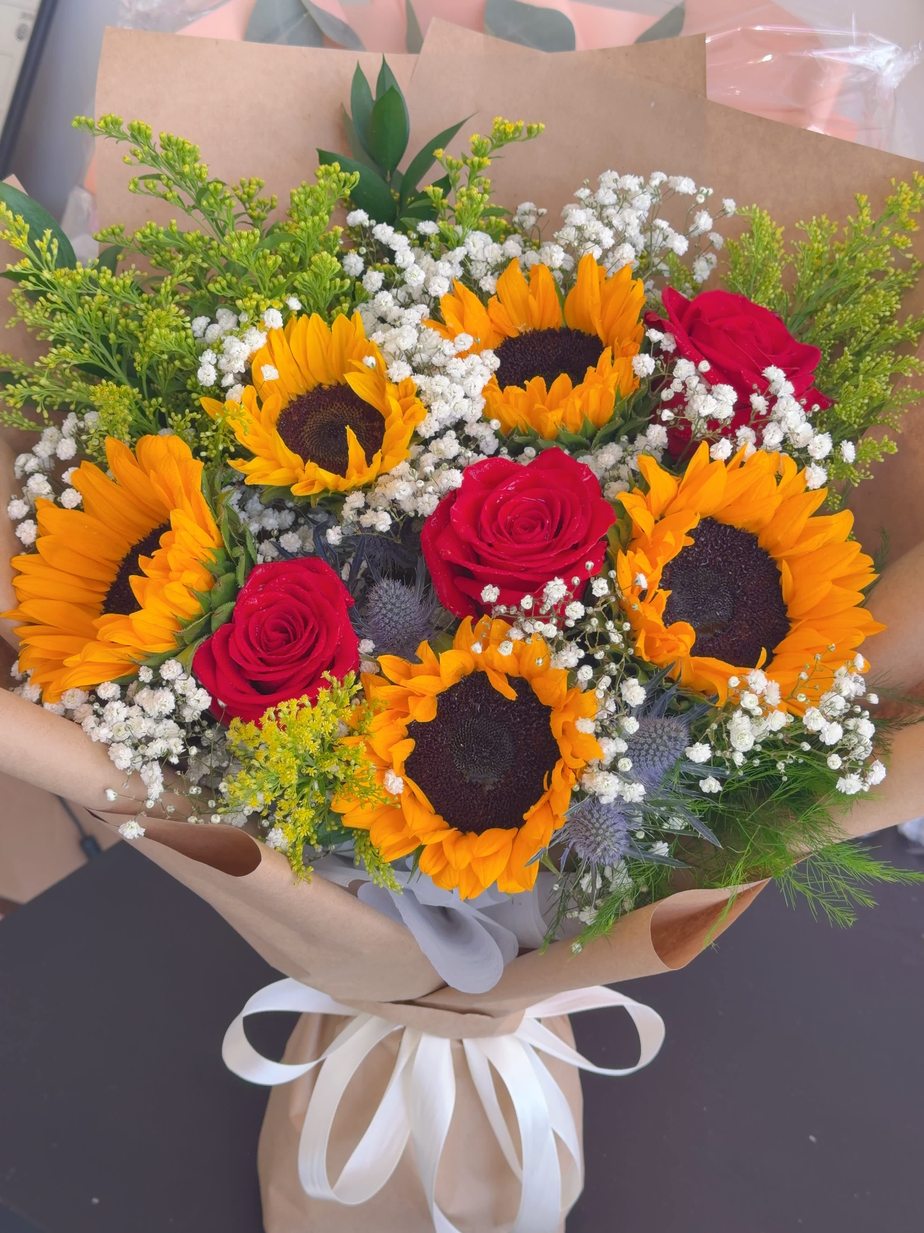 Bouquet of sunflowers and red roses wrapped in brown paper