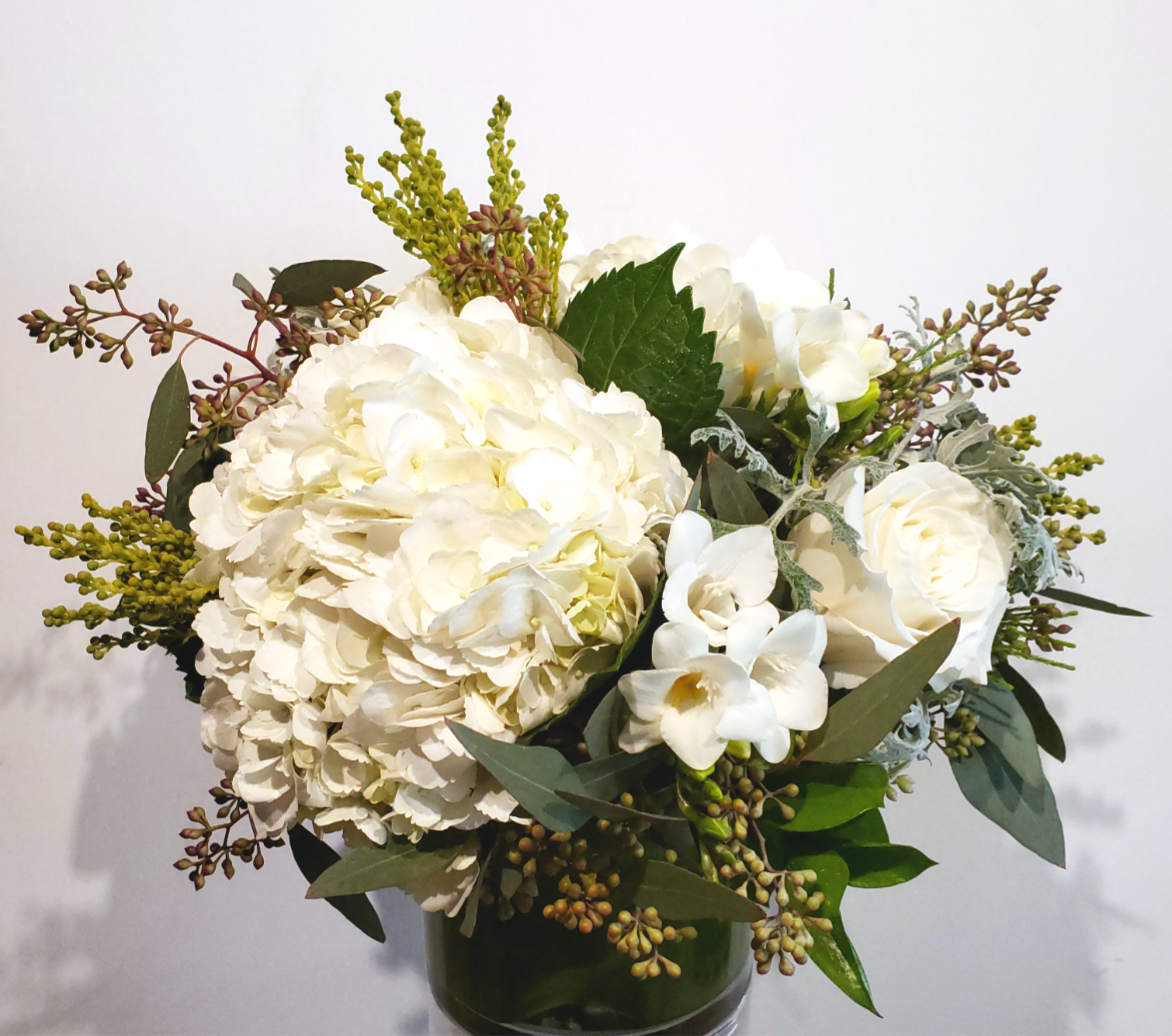 White hydrangeas and roses in a glass vase with mixed greenery