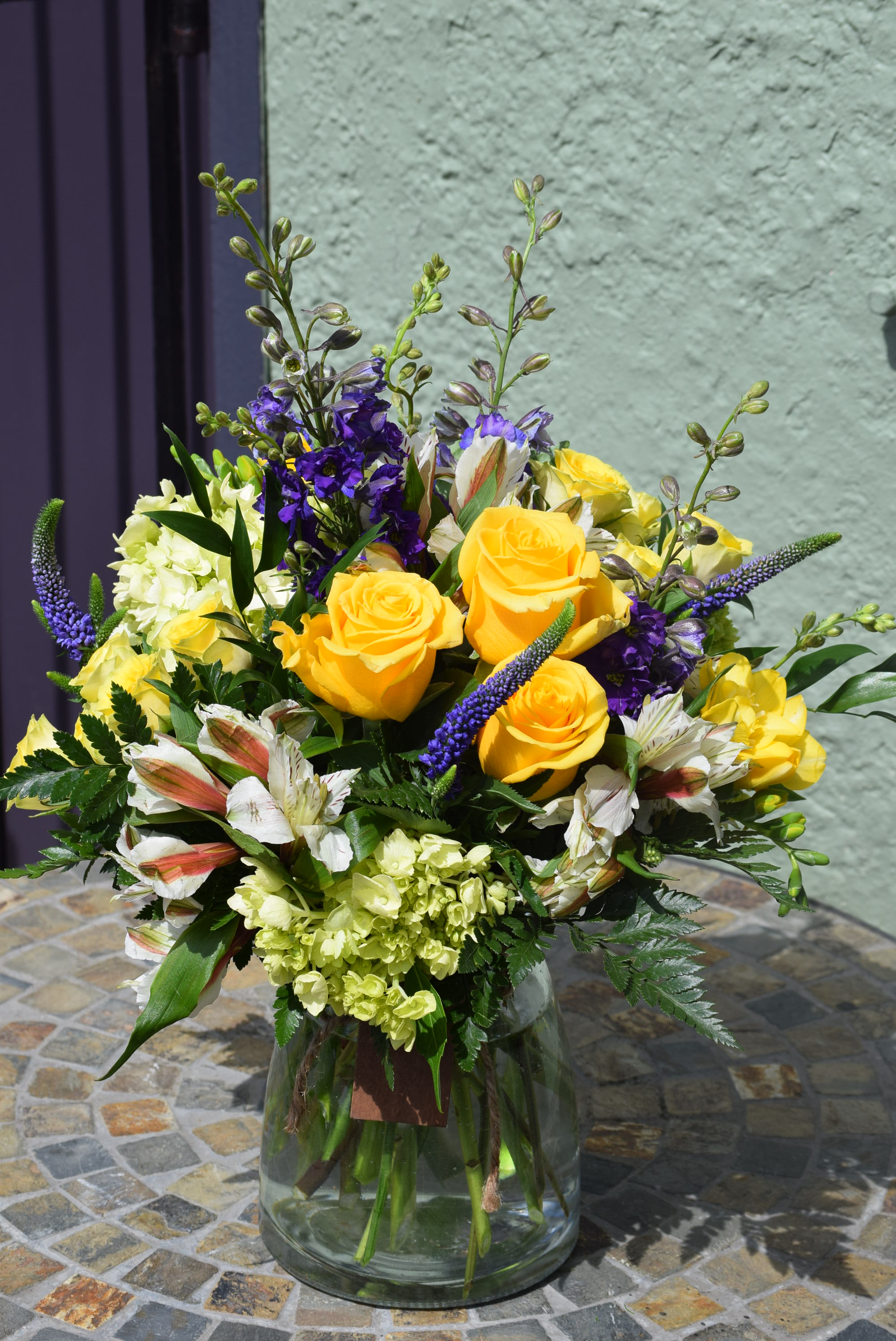 Yellow rose and purple flower arrangement with white blooms in a clear glass vase on a mosaic table