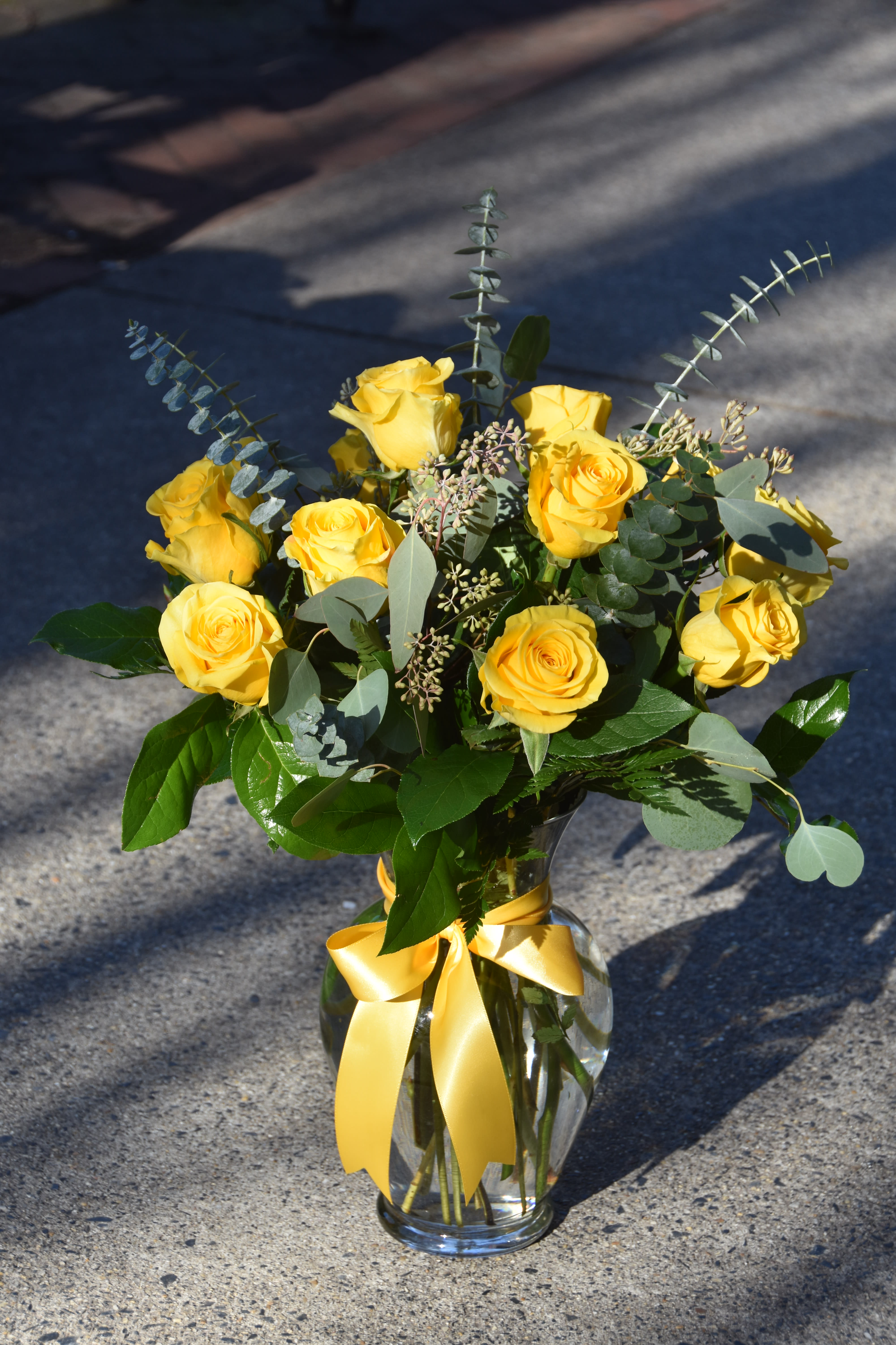 Arrangement of yellow roses with a yellow ribbon bow in a clear glass vase.