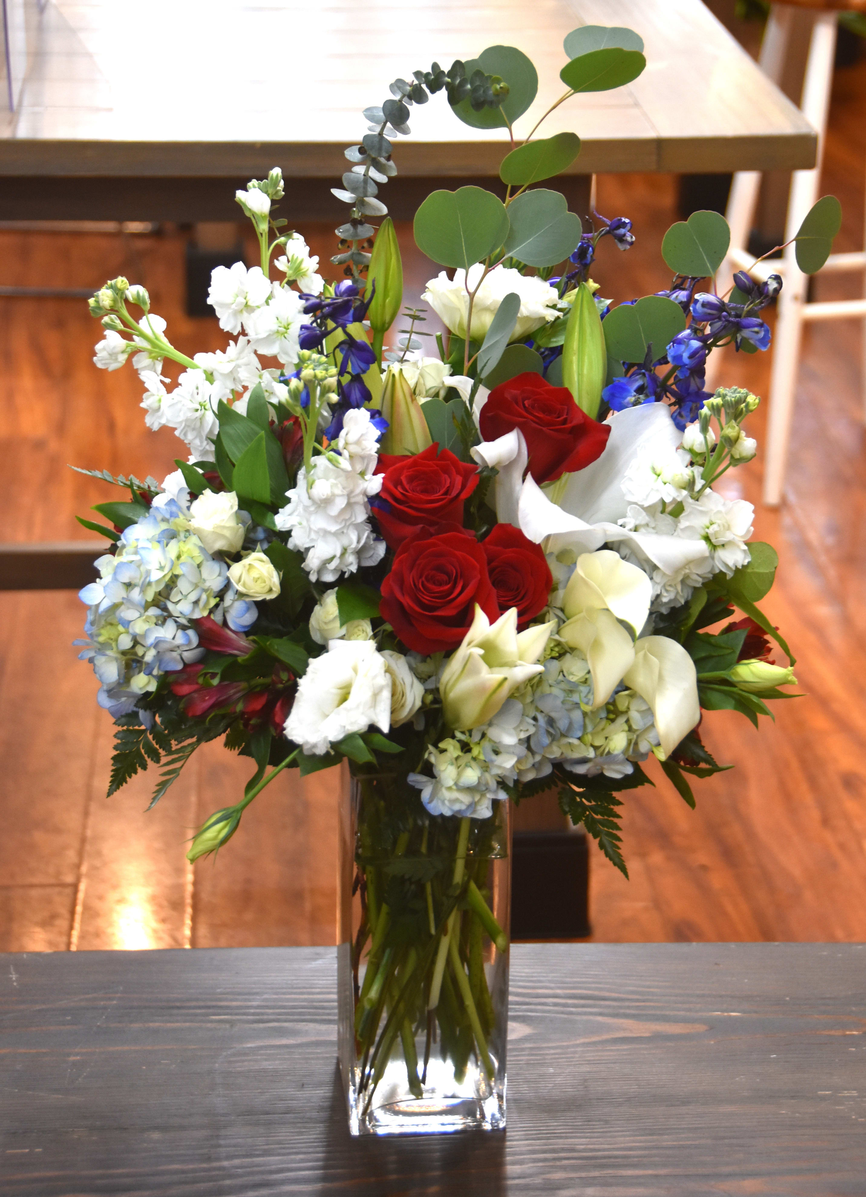 Tall red, white, and blue mixed flower arrangement in a clear rectangular glass vase