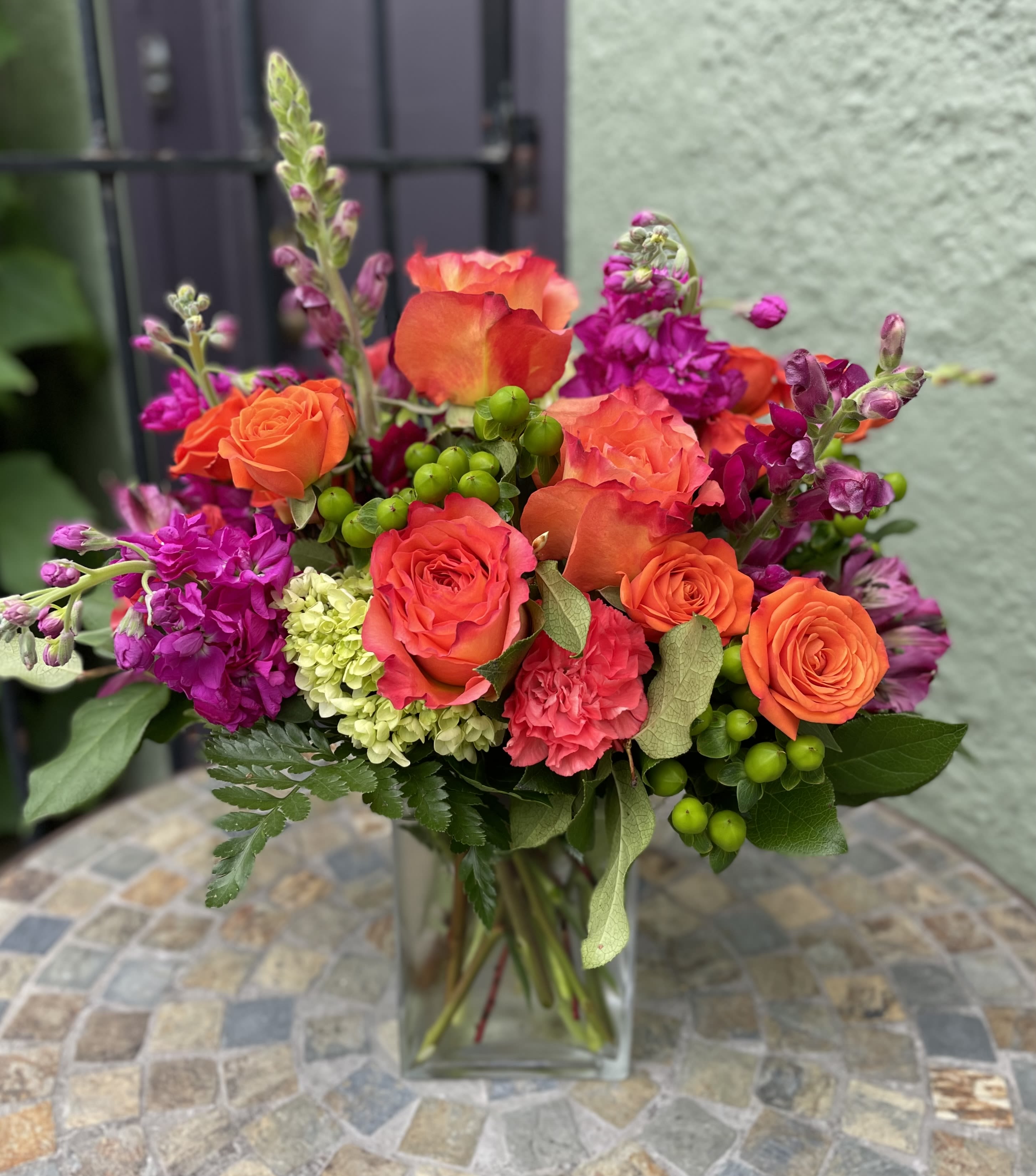 Bright arrangement of orange roses and pink flowers in a clear glass vase on a mosaic table