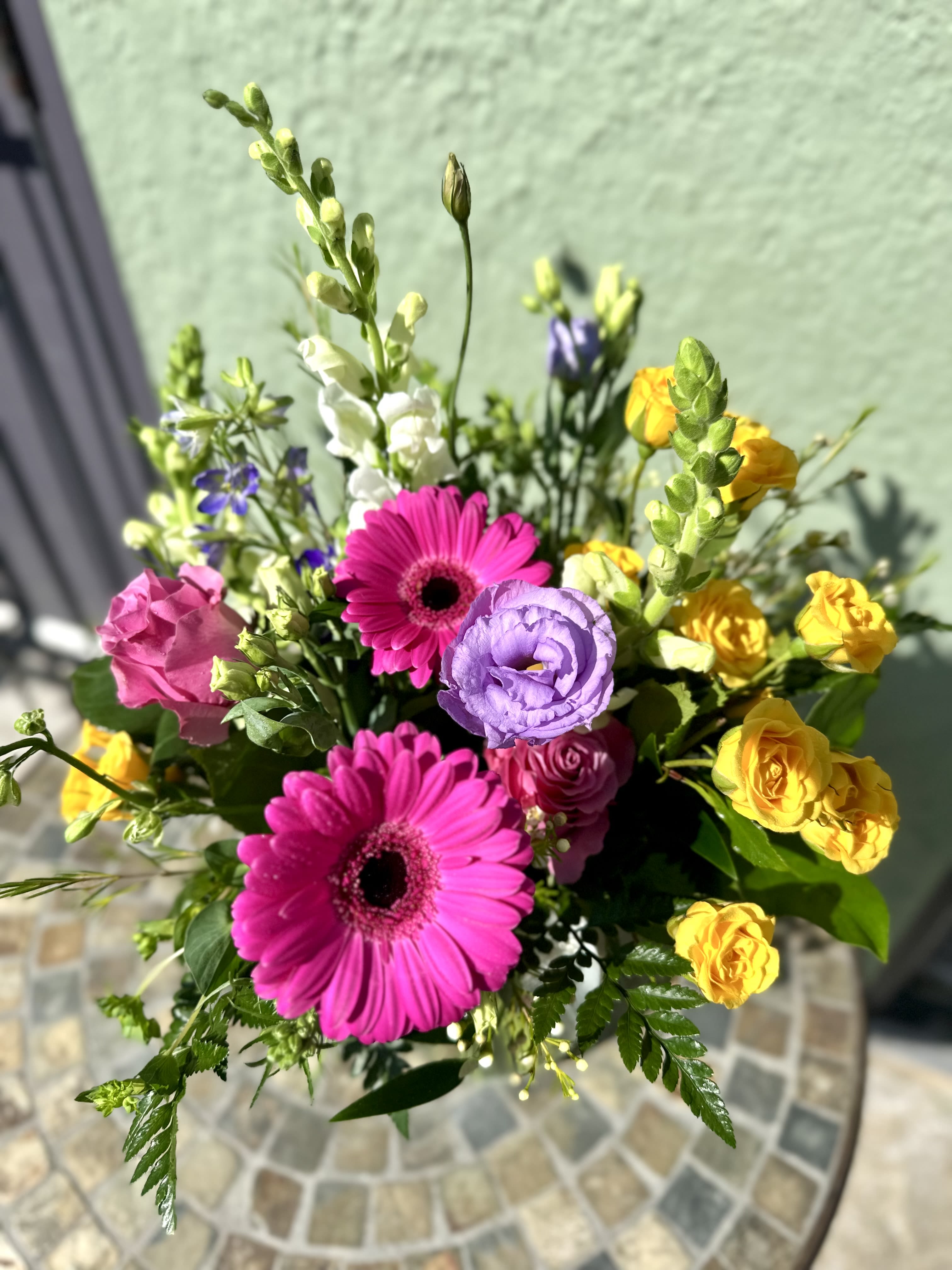 Bright bouquet with hot pink gerbera daisies, yellow spray roses, purple lisianthus, and white snapdragons