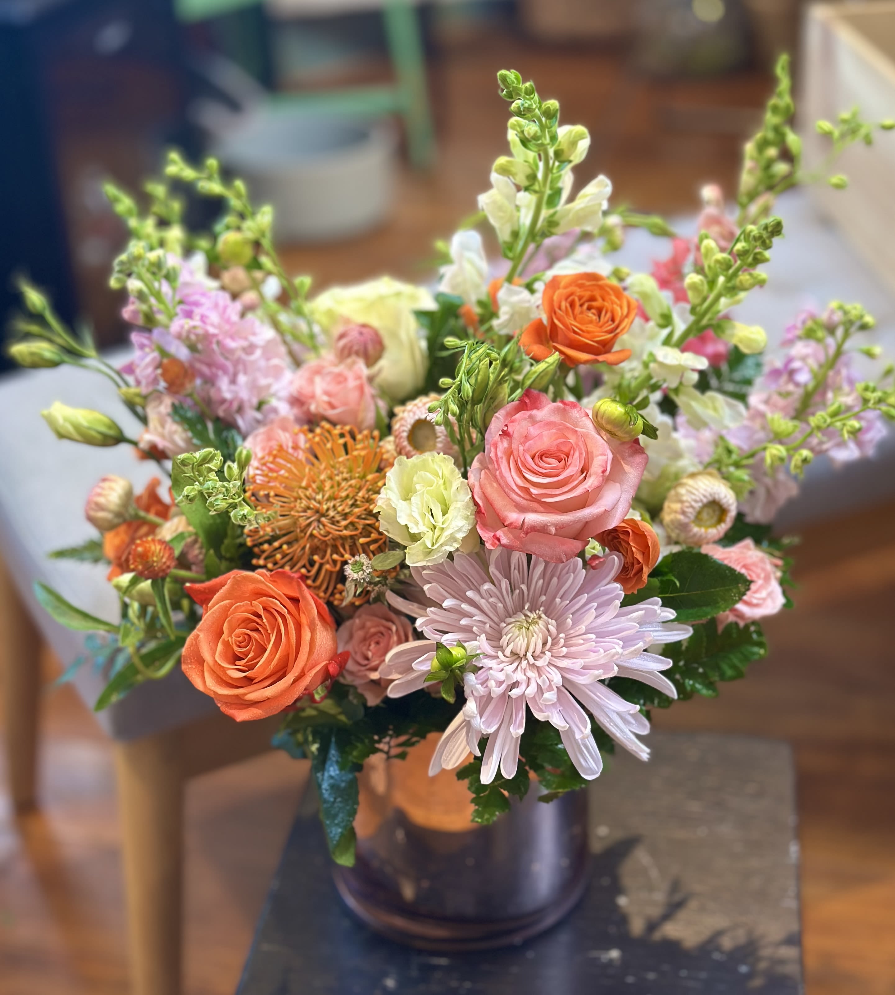 Mixed arrangement of pink and orange roses, mums, and snapdragons in a metallic vase