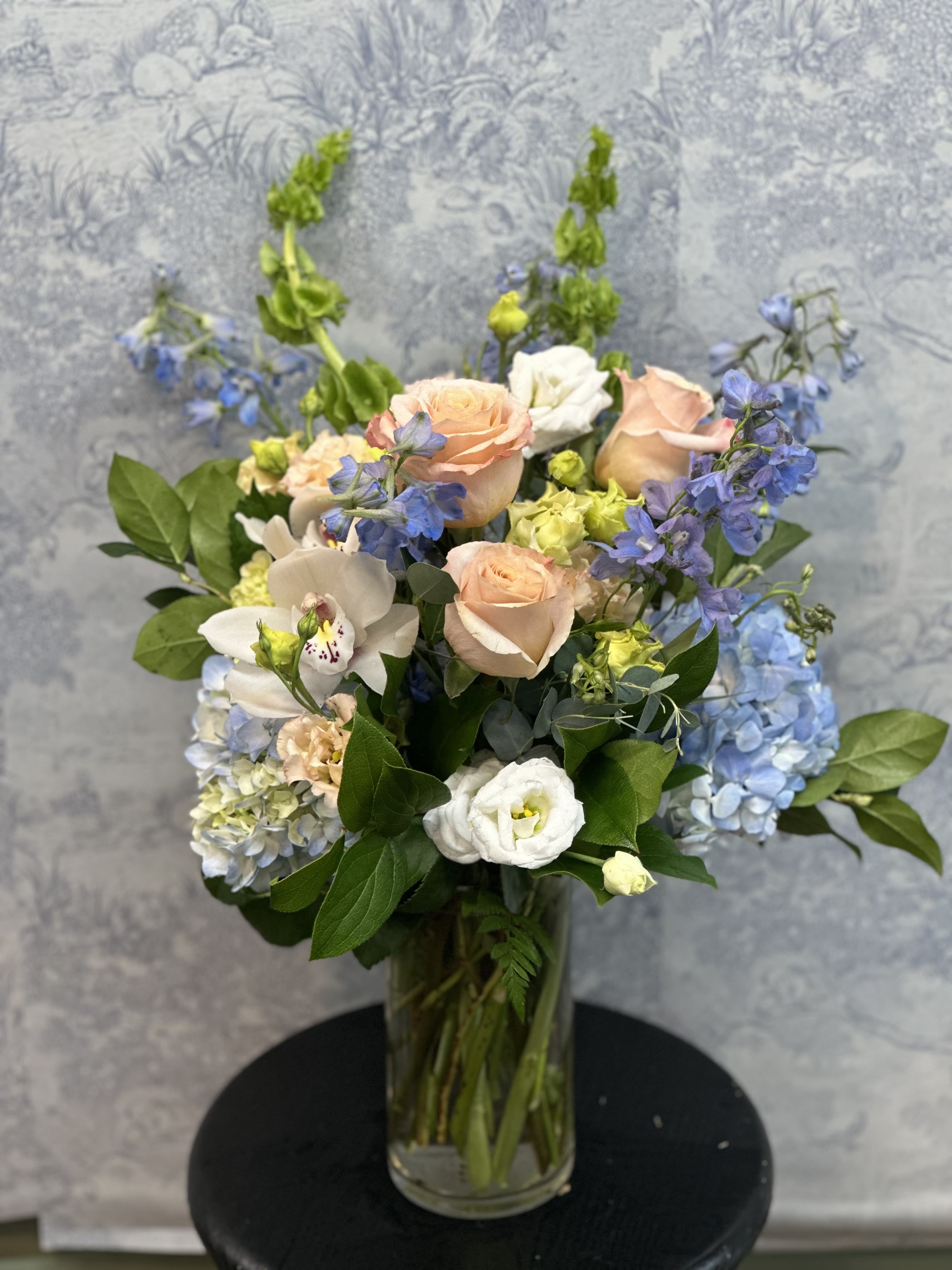 Shimmering Sky - Shimmering Sky captures the soft beauty of a pastel horizon, blending blue and white flowers with gorgeous Shimmer roses  into an arrangement that feels light and dreamy. This design brings a sense of calm beauty and quiet celebration to any space.