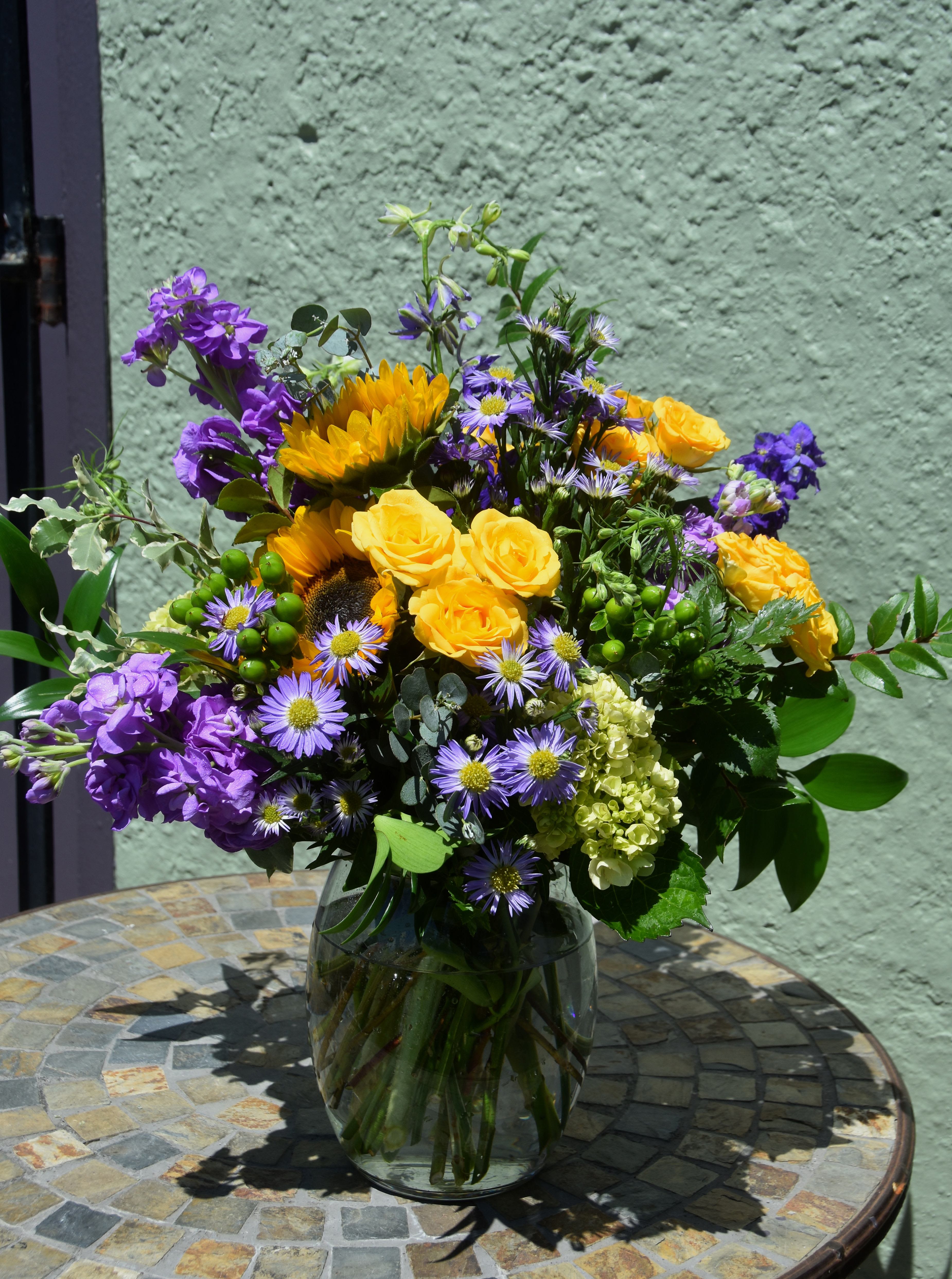 Saturday in the Park - Celebrate the spirit of summer with Saturday in the Park, a joyful arrangement overflowing with sunflowers, yellow and purple blooms, and lush greenery. Lively and full of feel-good energy just like its namesake song, this design the perfect way to make any day of the week feel a little more special.