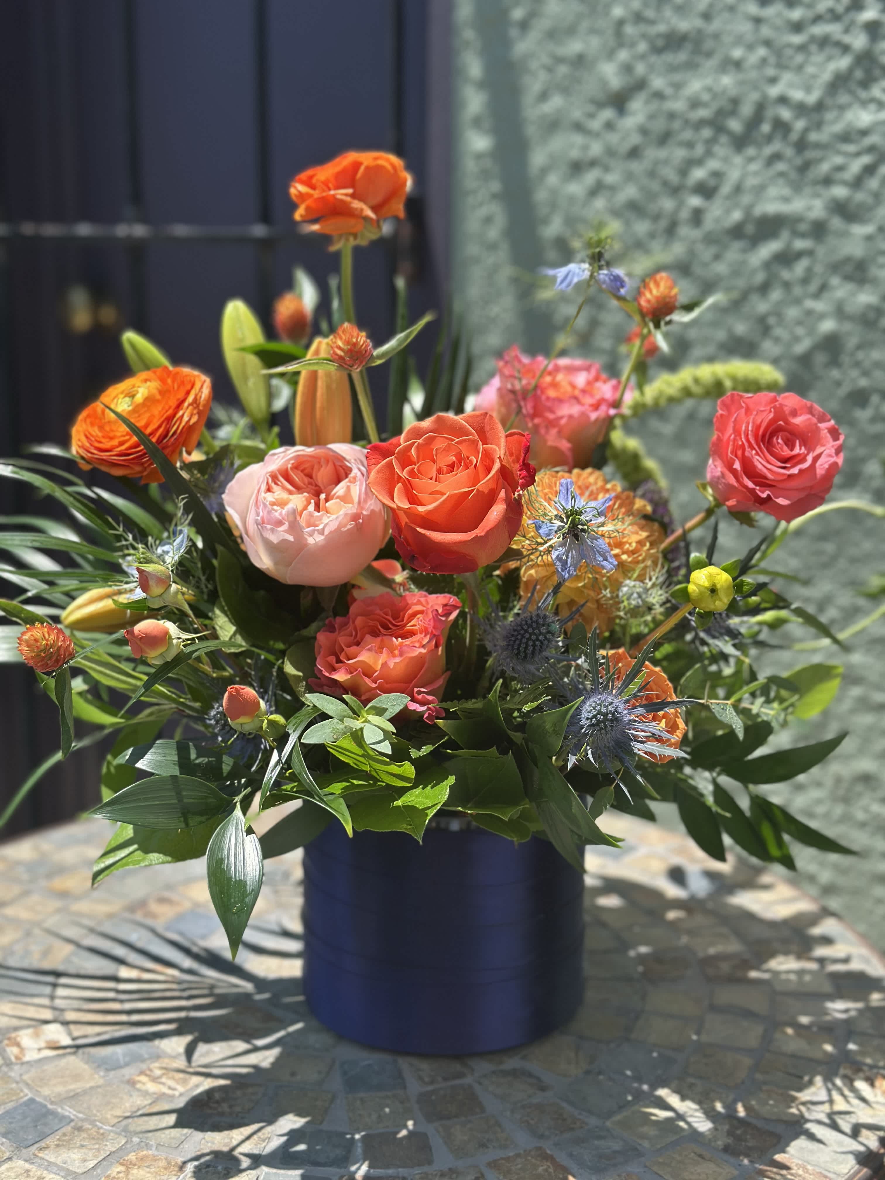 Colorful mixed bouquet in a dark blue vase with orange and pink roses