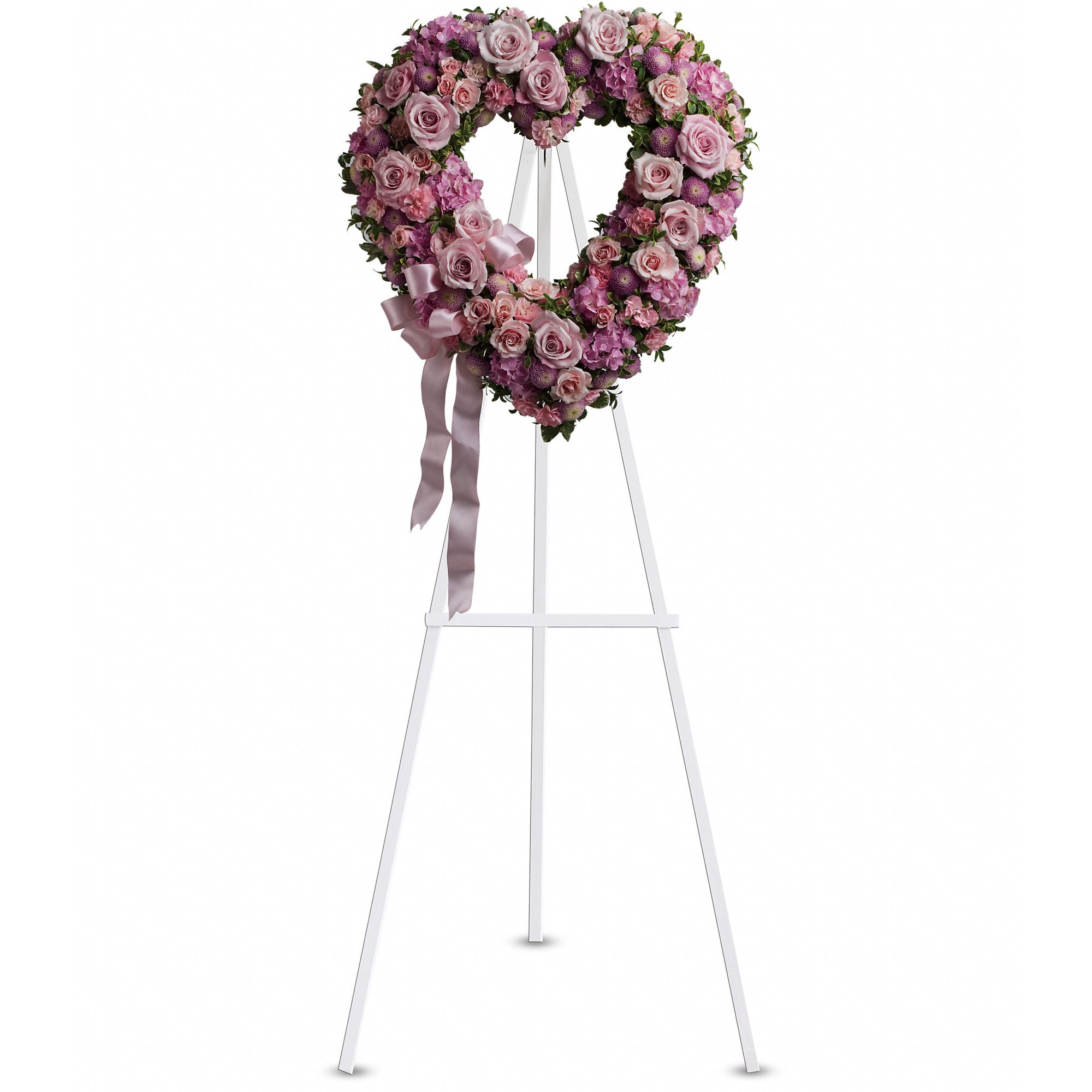 Heart-shaped wreath of pink and lavender roses on a white standing easel with a satin ribbon bow.