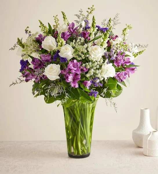 White roses and purple flowers in a tall glass vase