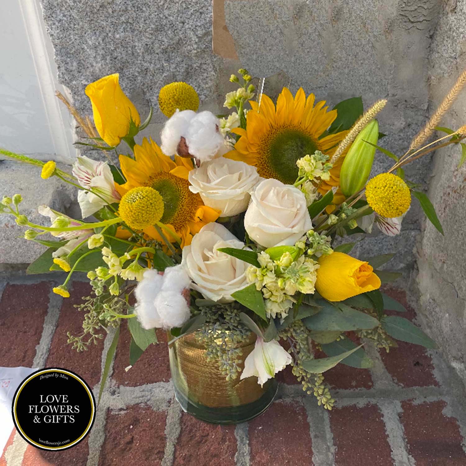 Vase arrangement of yellow sunflowers, white roses, and yellow tulips in a glass cylinder vase