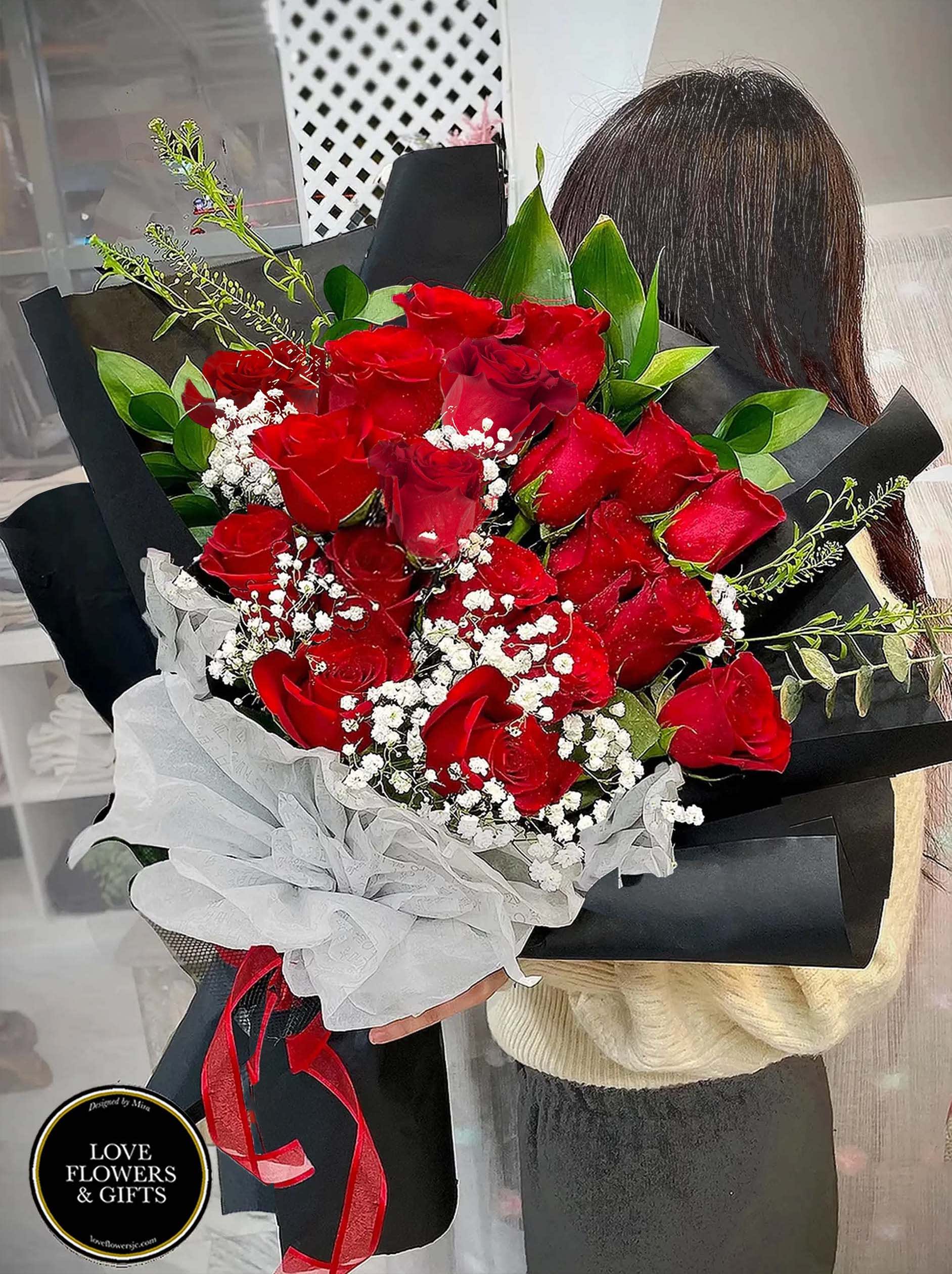 Large hand-tied bouquet of red roses with white filler flowers wrapped in black paper and white tissue.