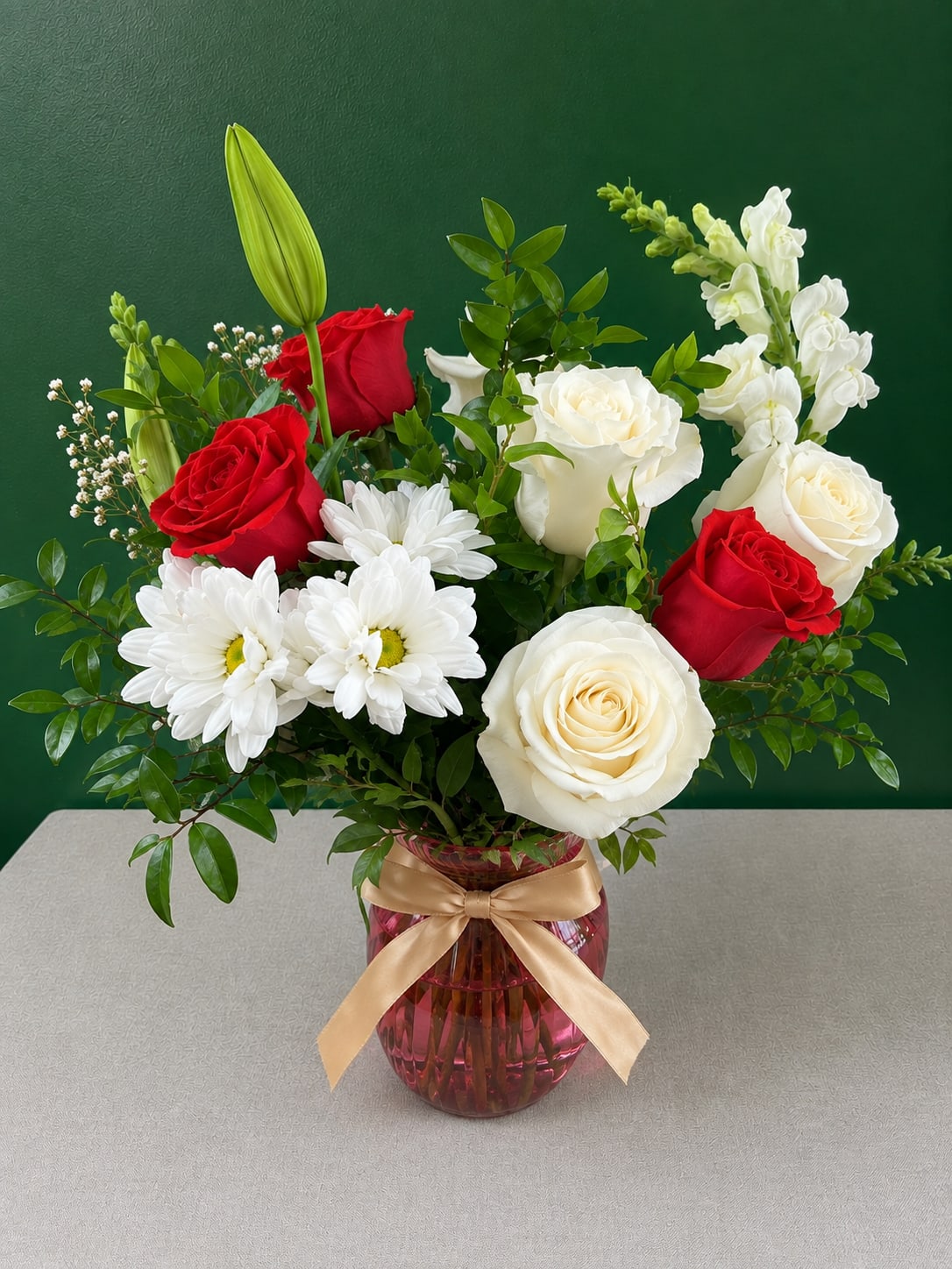 Red and white roses with daisies in a pink vase with a gold ribbon