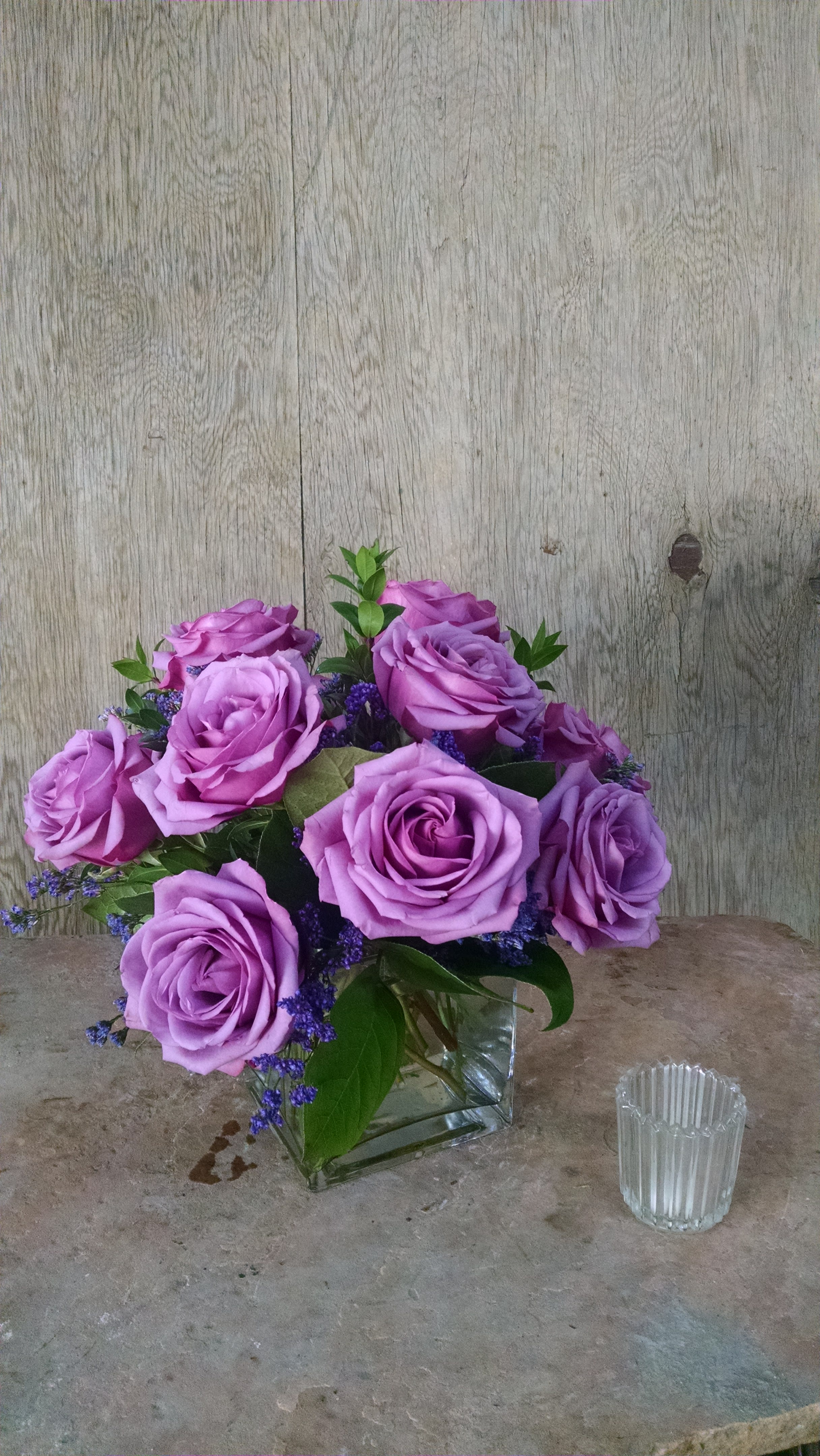 Lavender rose bouquet in a clear square vase with purple filler flowers