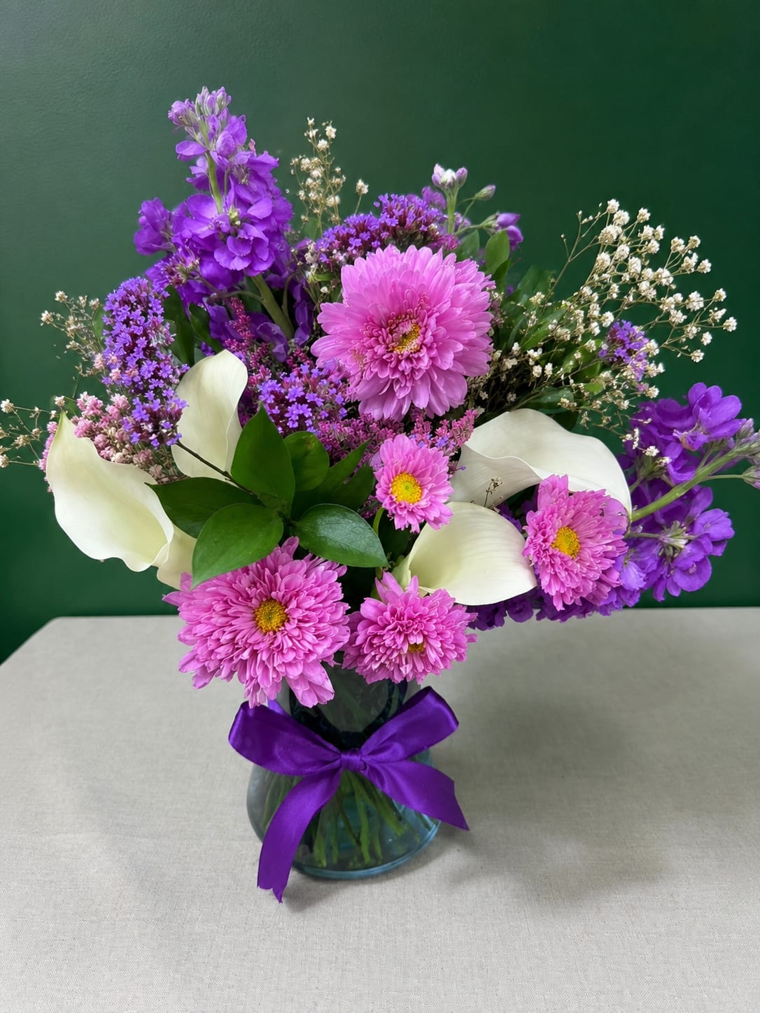 Purple and pink mixed bouquet with white calla lilies in a glass vase
