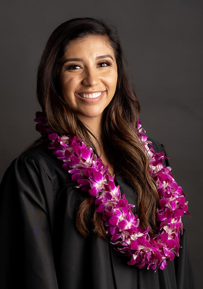 Woman wearing a purple orchid lei over a black graduation gown