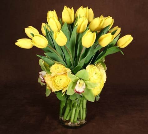 Yellow tulips and roses arranged in a clear glass vase