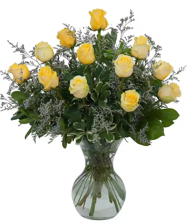 Yellow roses arranged in a clear glass vase with greenery
