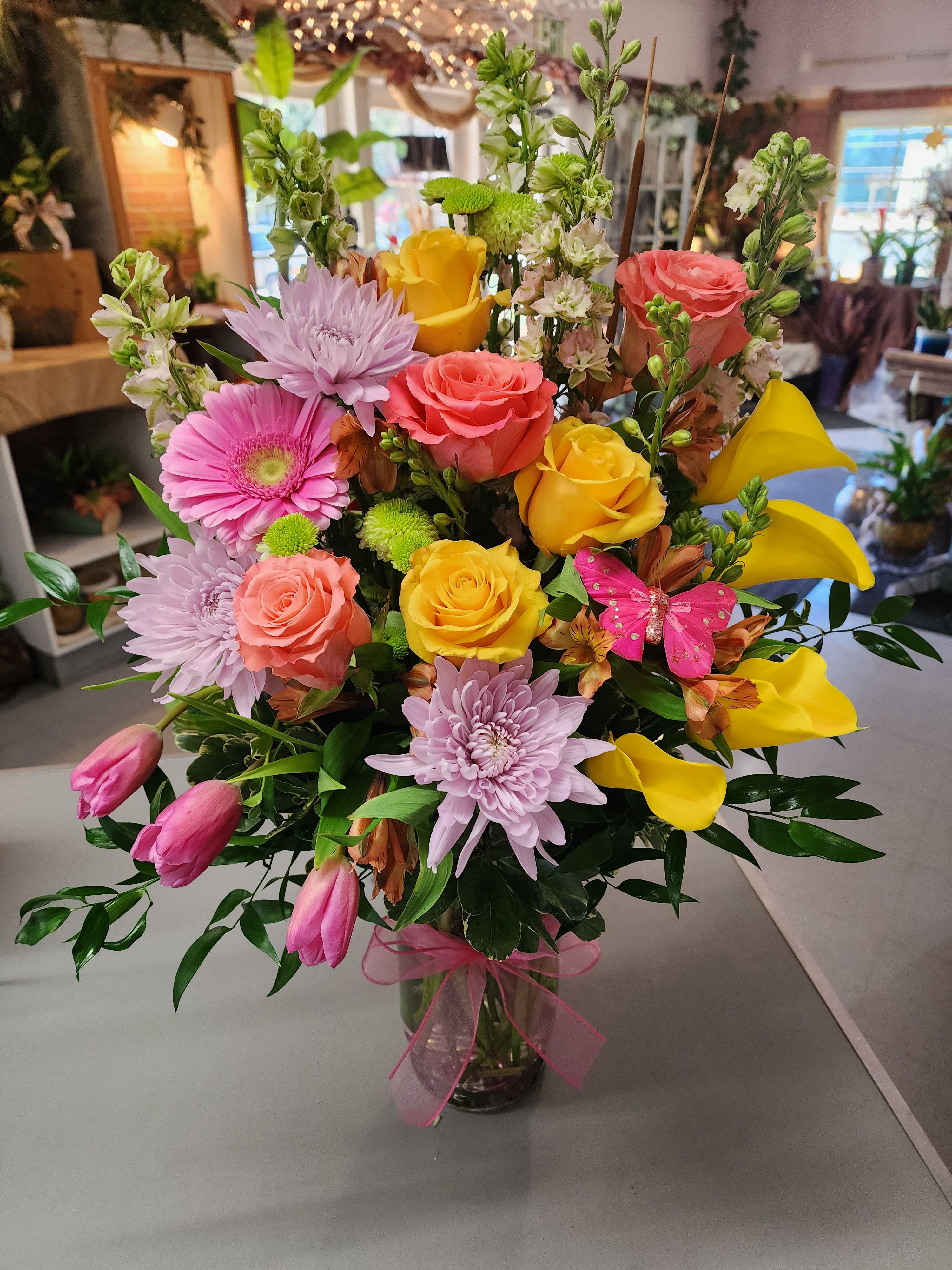 Calla Surprise - A Calla Lily and Tulip arrangement is a beautiful blend of elegance and charm. The sleek, trumpet-shaped Calla Lilies pair wonderfully with the soft, cup-shaped Tulips, creating a harmonious balance. These arrangements often feature complementary colors and flowers, such as Roses, Gerbera, larkspur and alstroemeria. This arrangement is enhanced with greenery like eucalyptus, ferns, and sometimes accented with delicate filler flowers. It's perfect for weddings, formal events, or as a sophisticated centerpiece. 