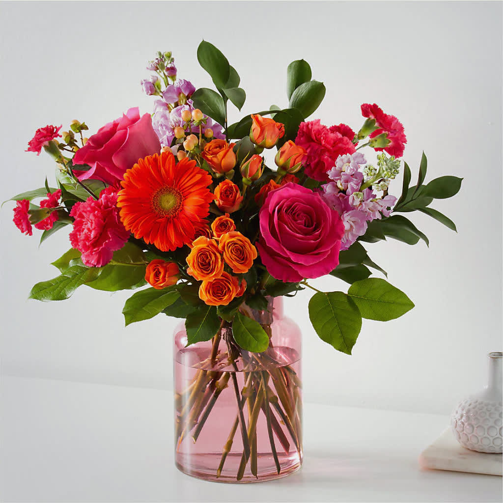 Bouquet of pink, orange, and red flowers in a pink glass vase