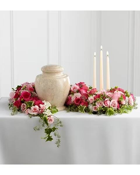 Pink rose arrangements around a beige urn with three candles