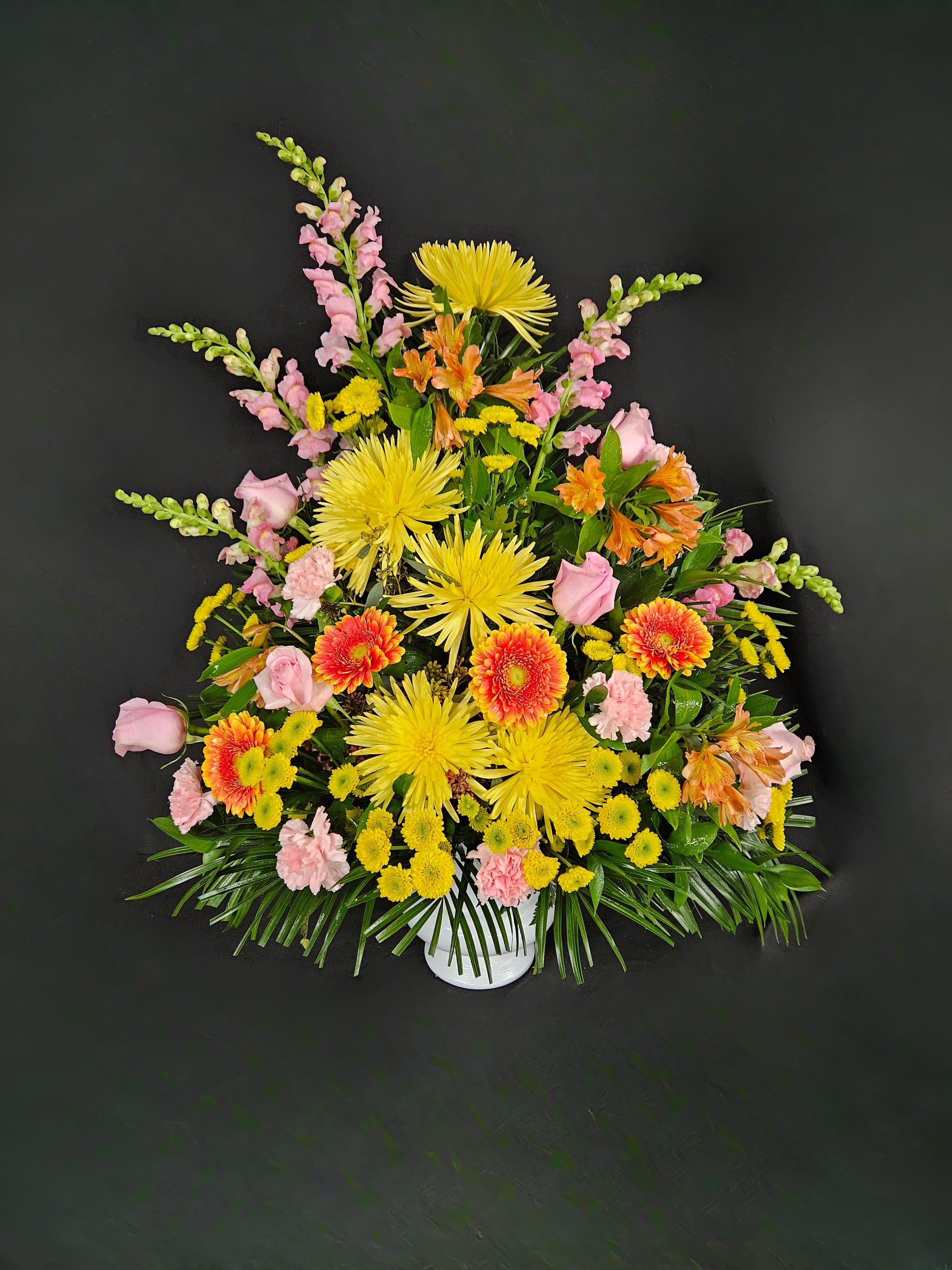 Tall fan-shaped arrangement of yellow and orange blooms with pink accents in a white container