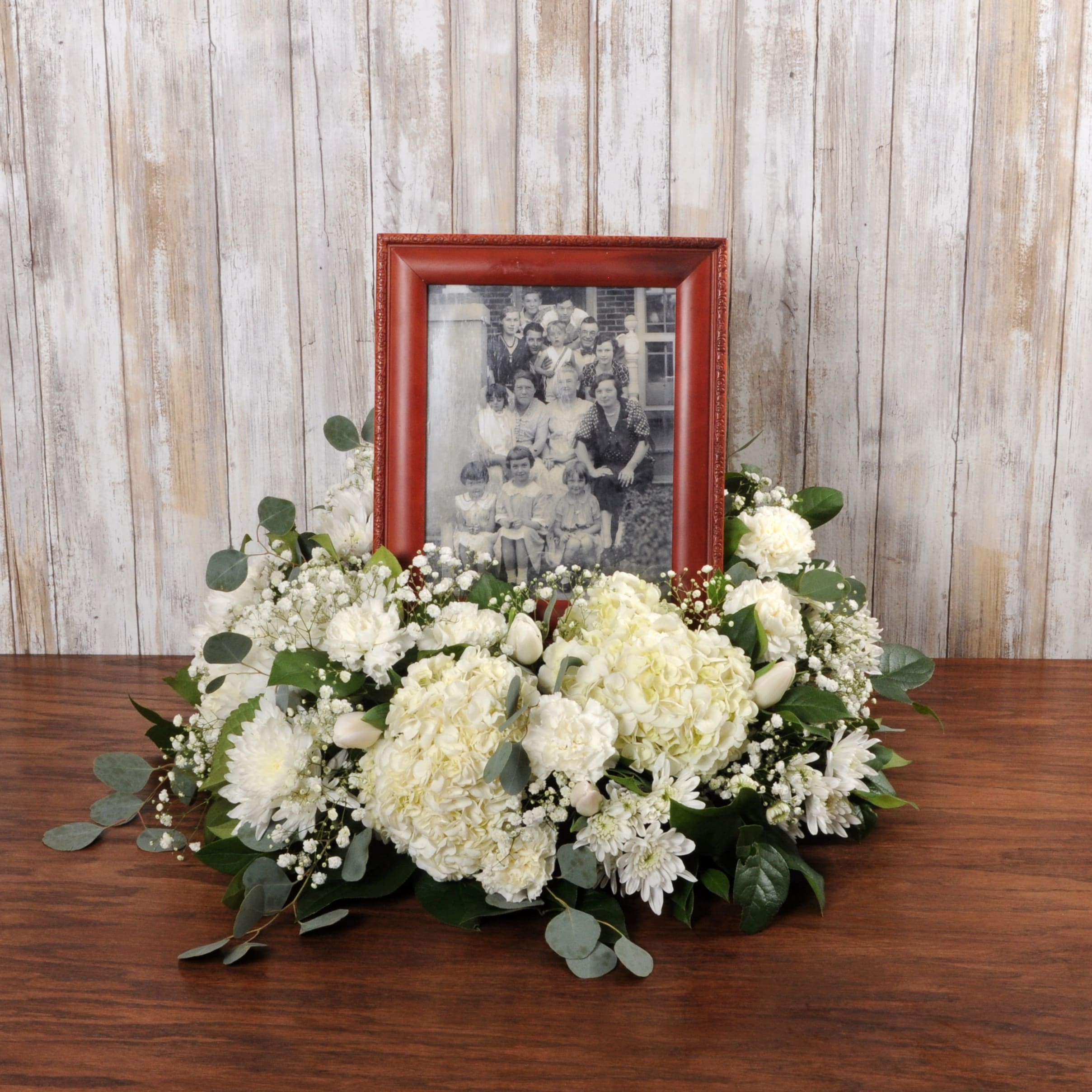 Low white floral arrangement surrounding a red photo frame with a black and white family picture.