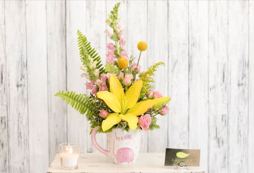 Yellow lily and pink flowers arranged in a mug with a baby girl design